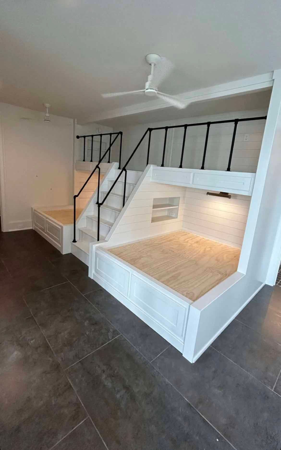 A room with bunk beds and stairs and a ceiling fan.