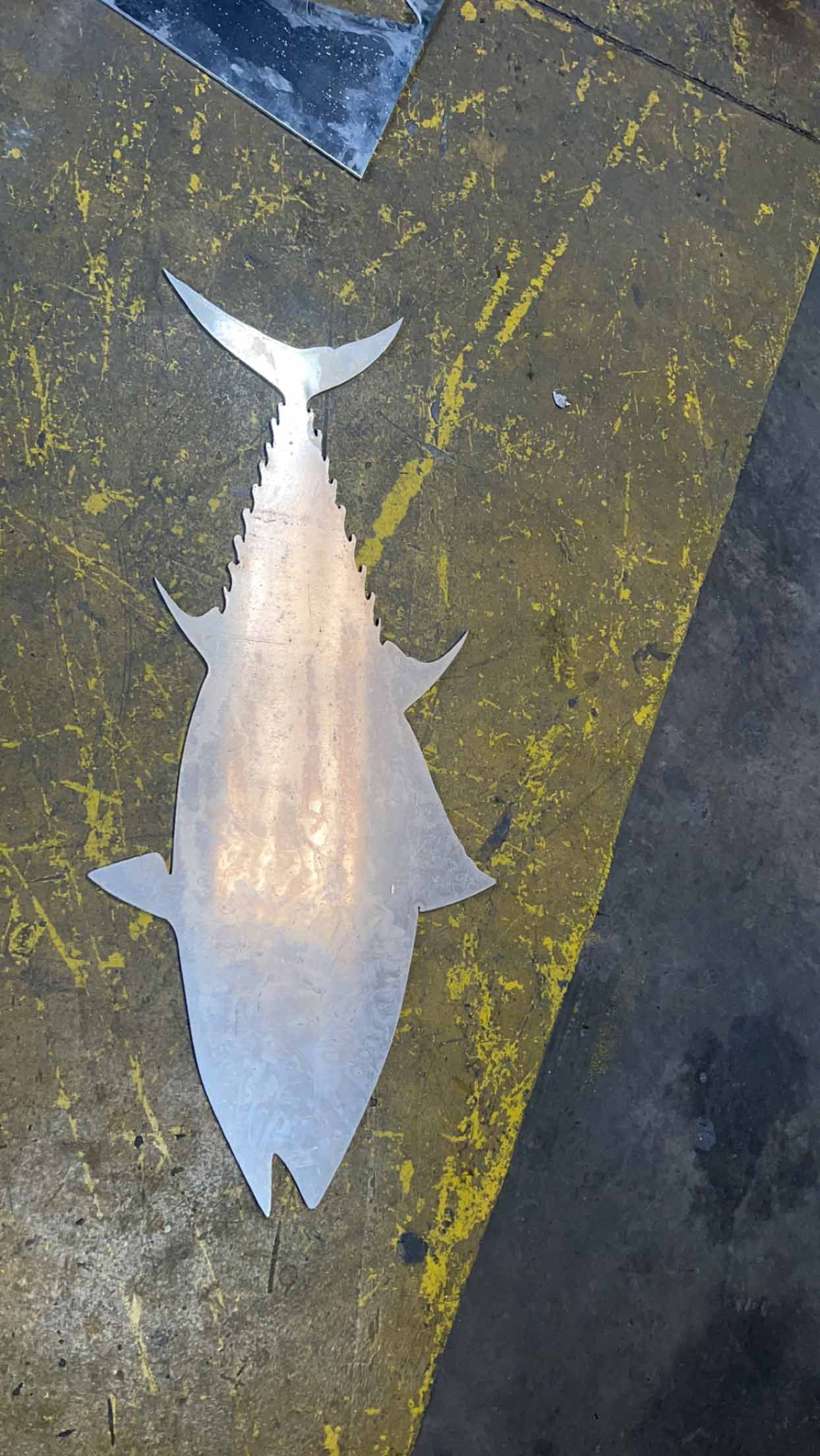A silhouette of a fish is sitting on a concrete surface.