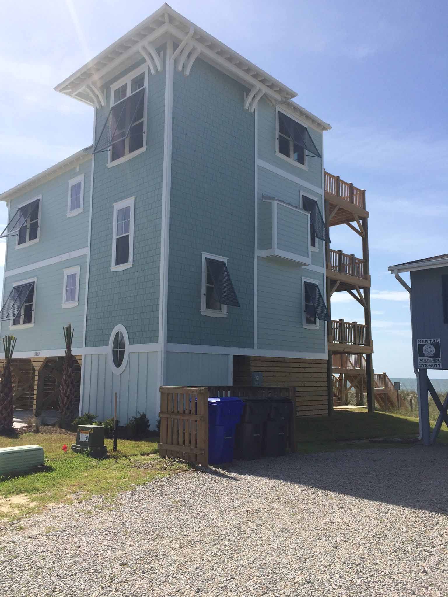 A large blue and white house with stairs is sitting on top of a gravel hill.