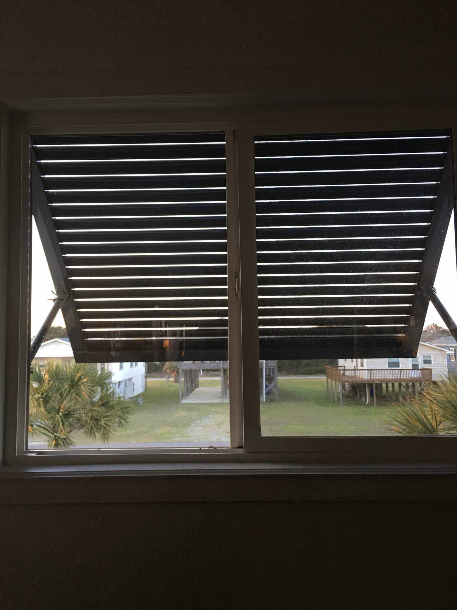 A window with shutters open and a view of a yard.