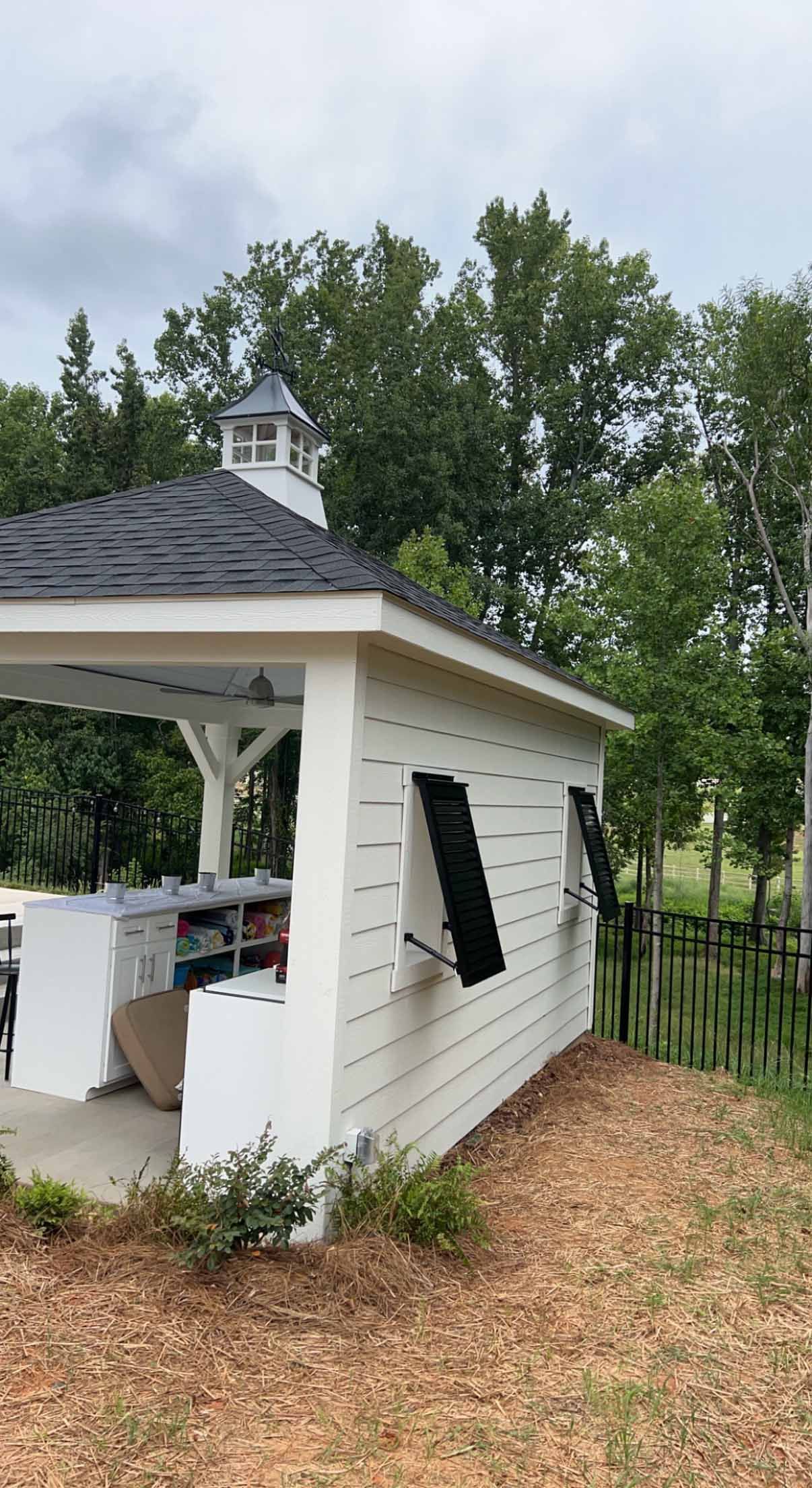 A white gazebo with a black roof is sitting in the middle of a field.