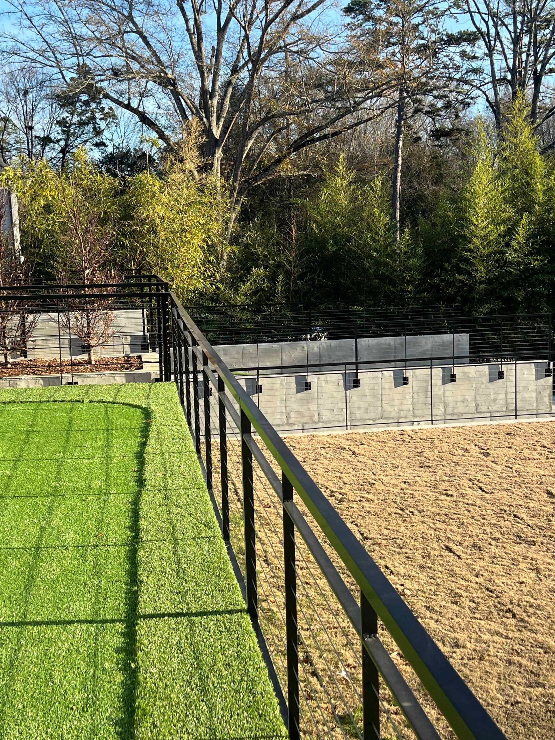 A fence surrounds a lush green field with trees in the background.