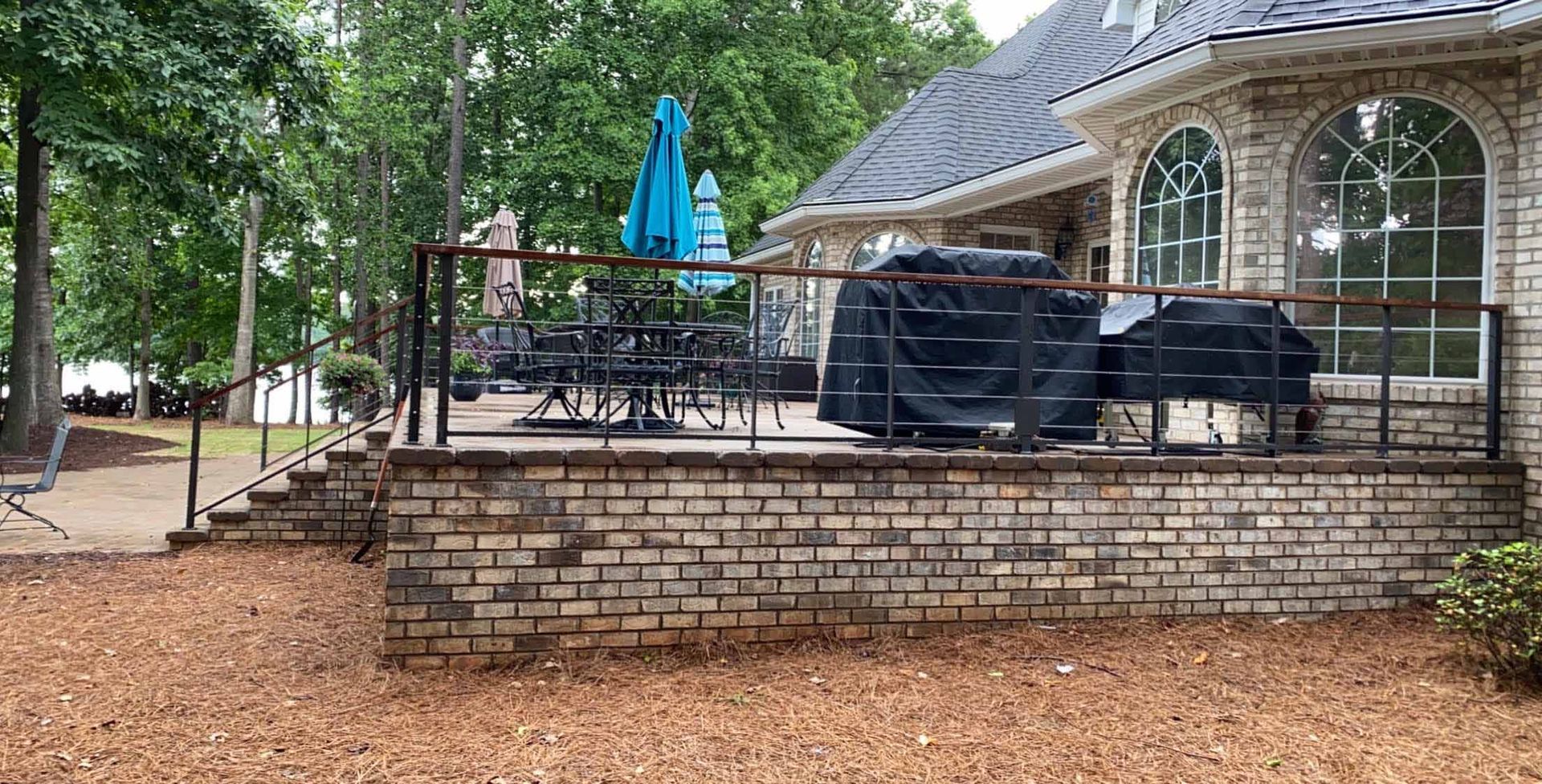 A brick deck with a grill and umbrellas in front of a house.