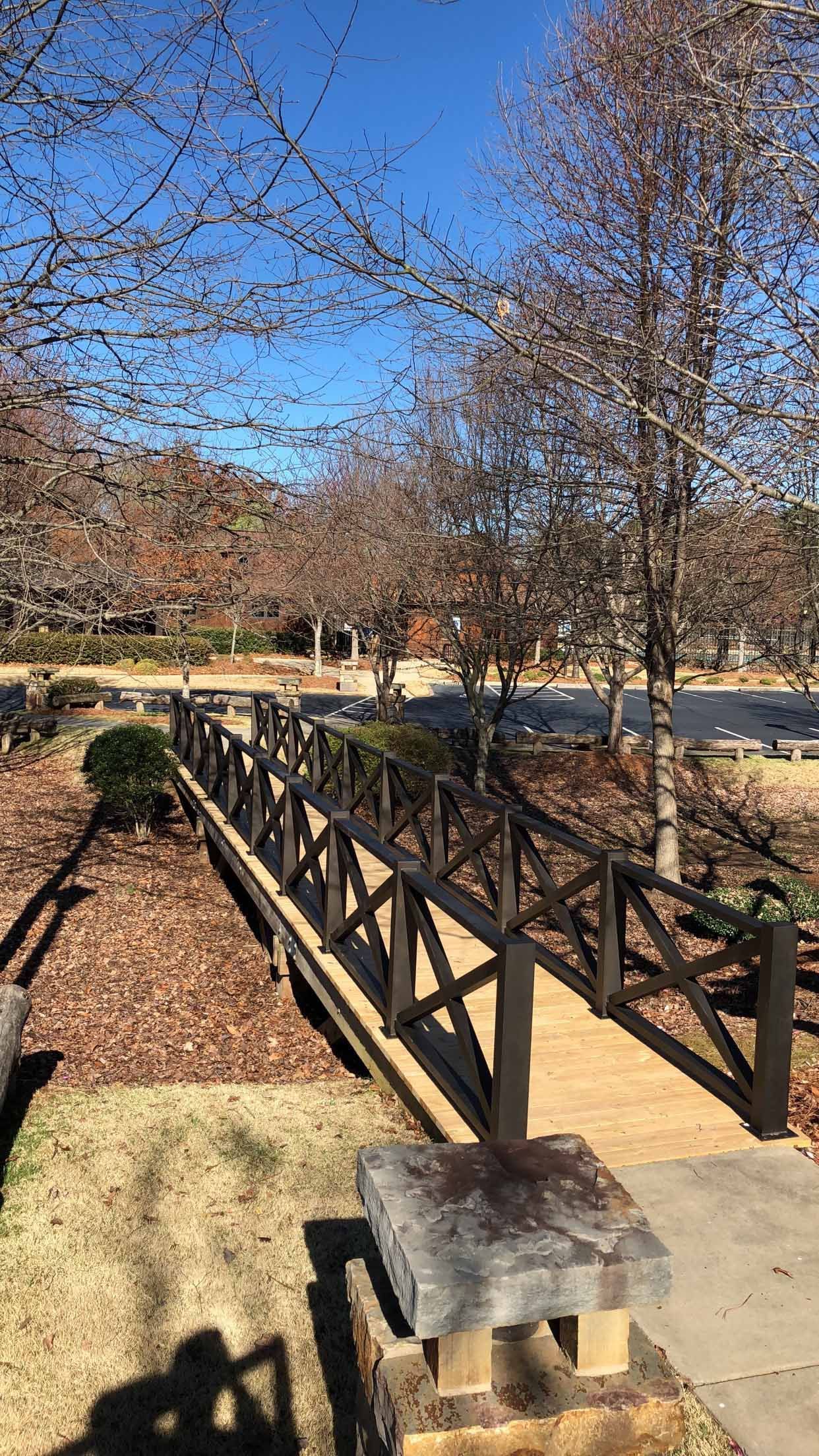 A wooden bridge over a river in a park with trees in the background.