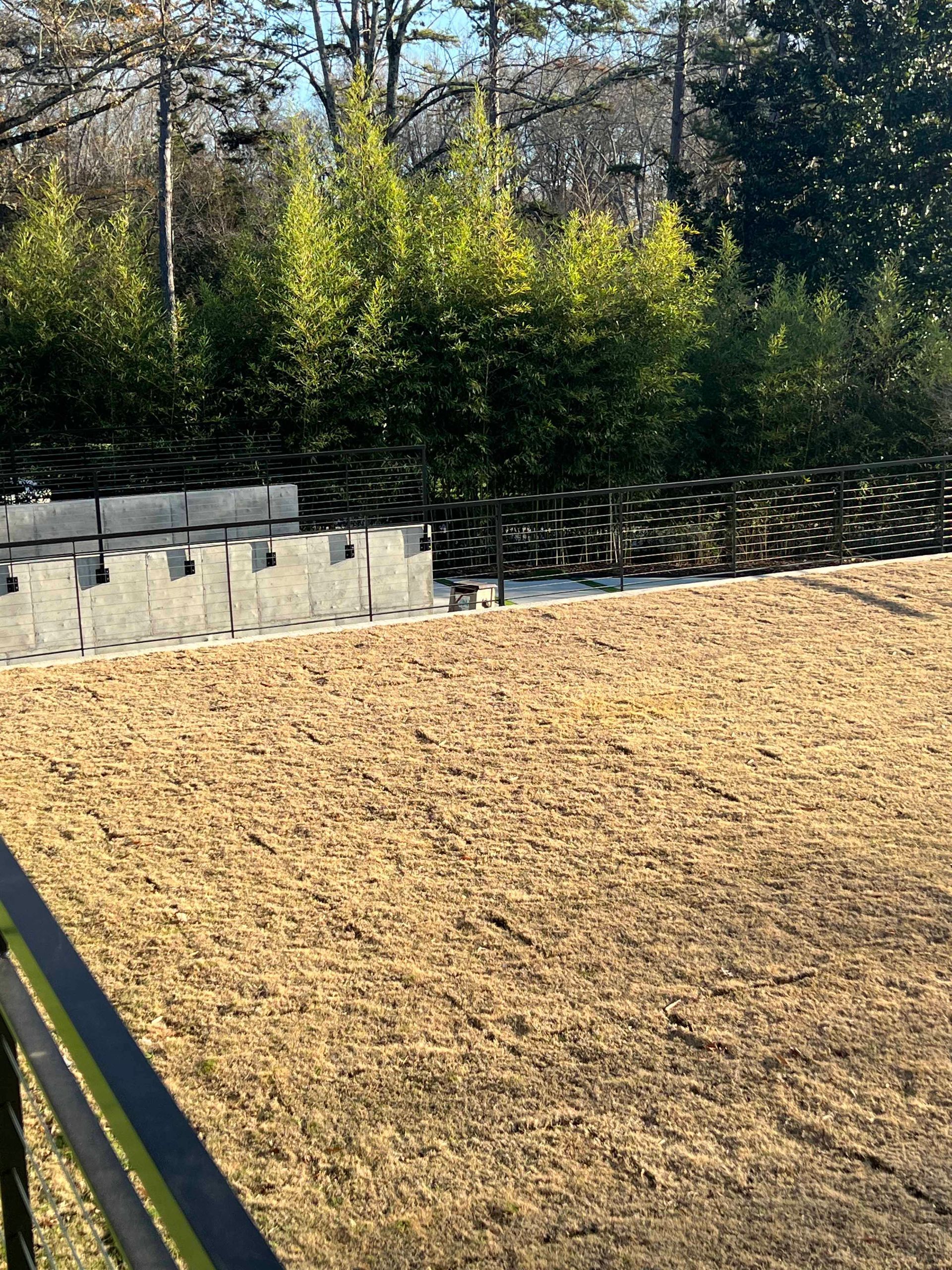 A dirt field with a fence and trees in the background.