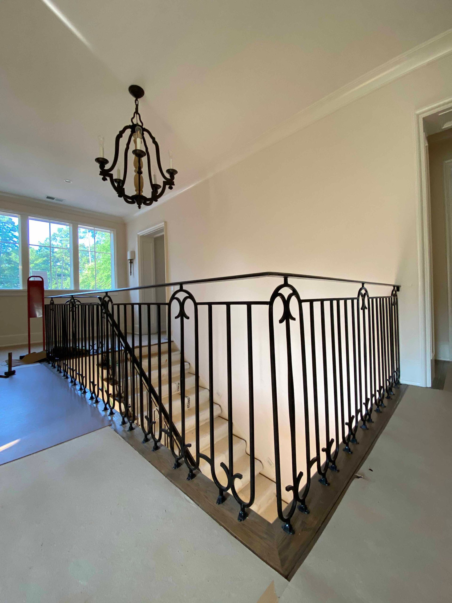 A staircase with a wrought iron railing and a chandelier hanging from the ceiling.
