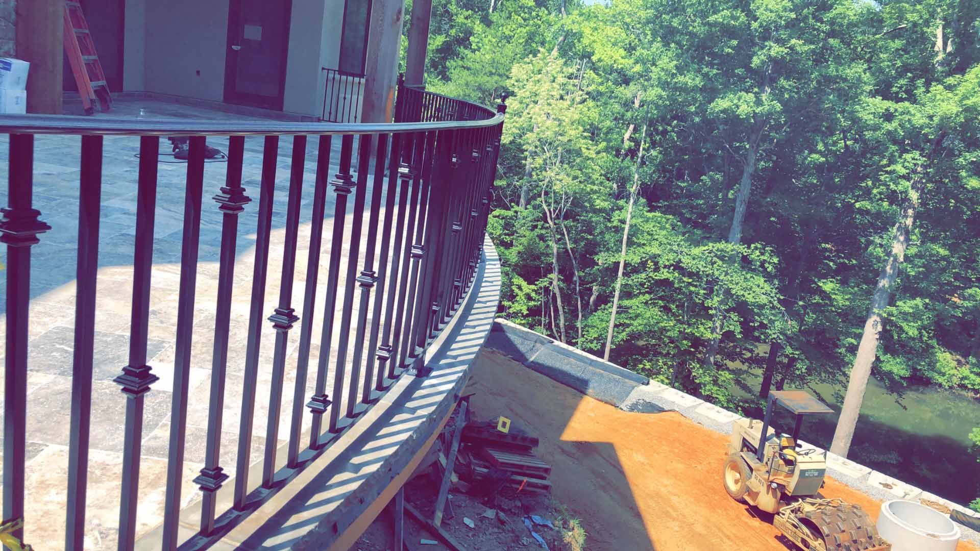 A balcony with a wrought iron railing and trees in the background.