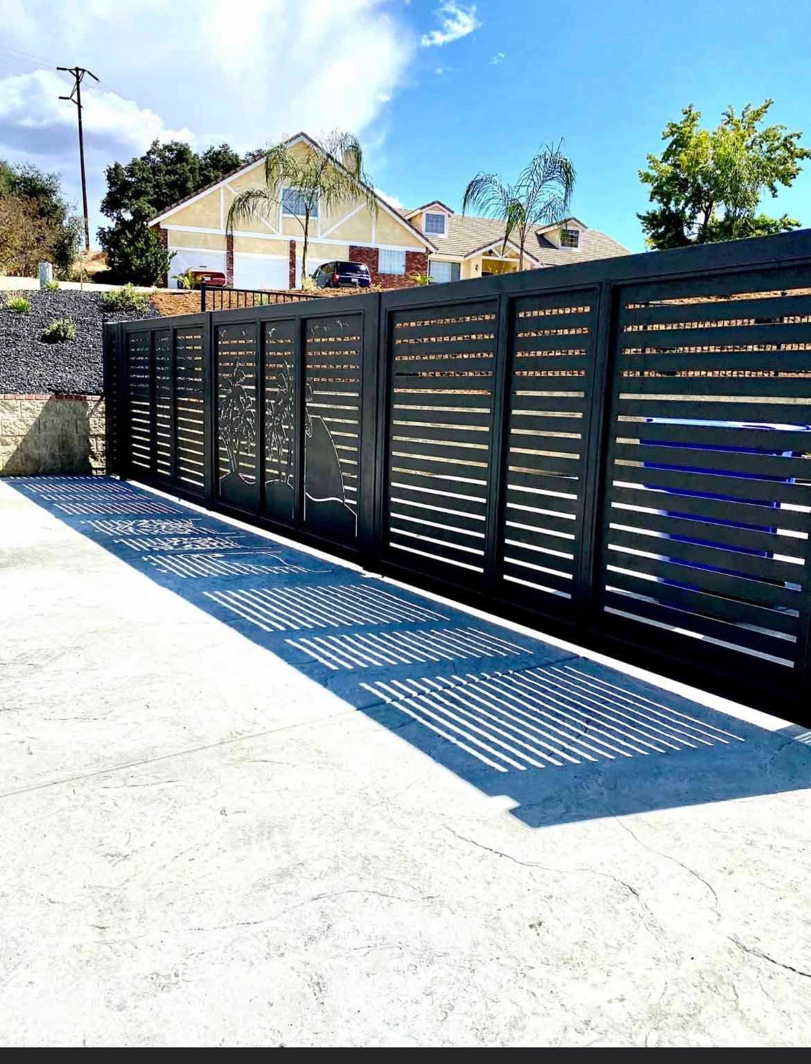 A black fence with a shadow on the ground in front of a house.