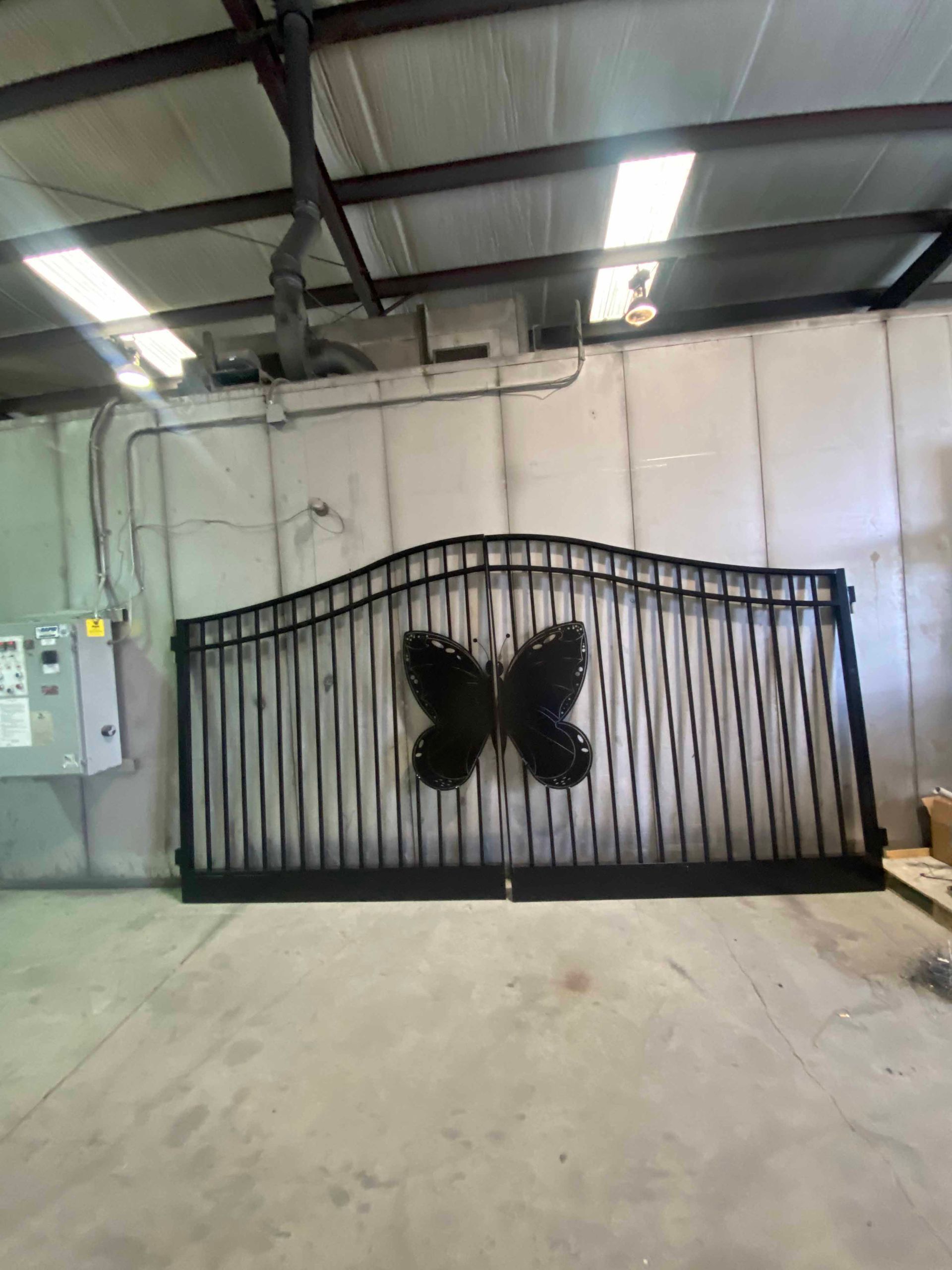 A wrought iron gate with a butterfly on it is sitting in a warehouse.