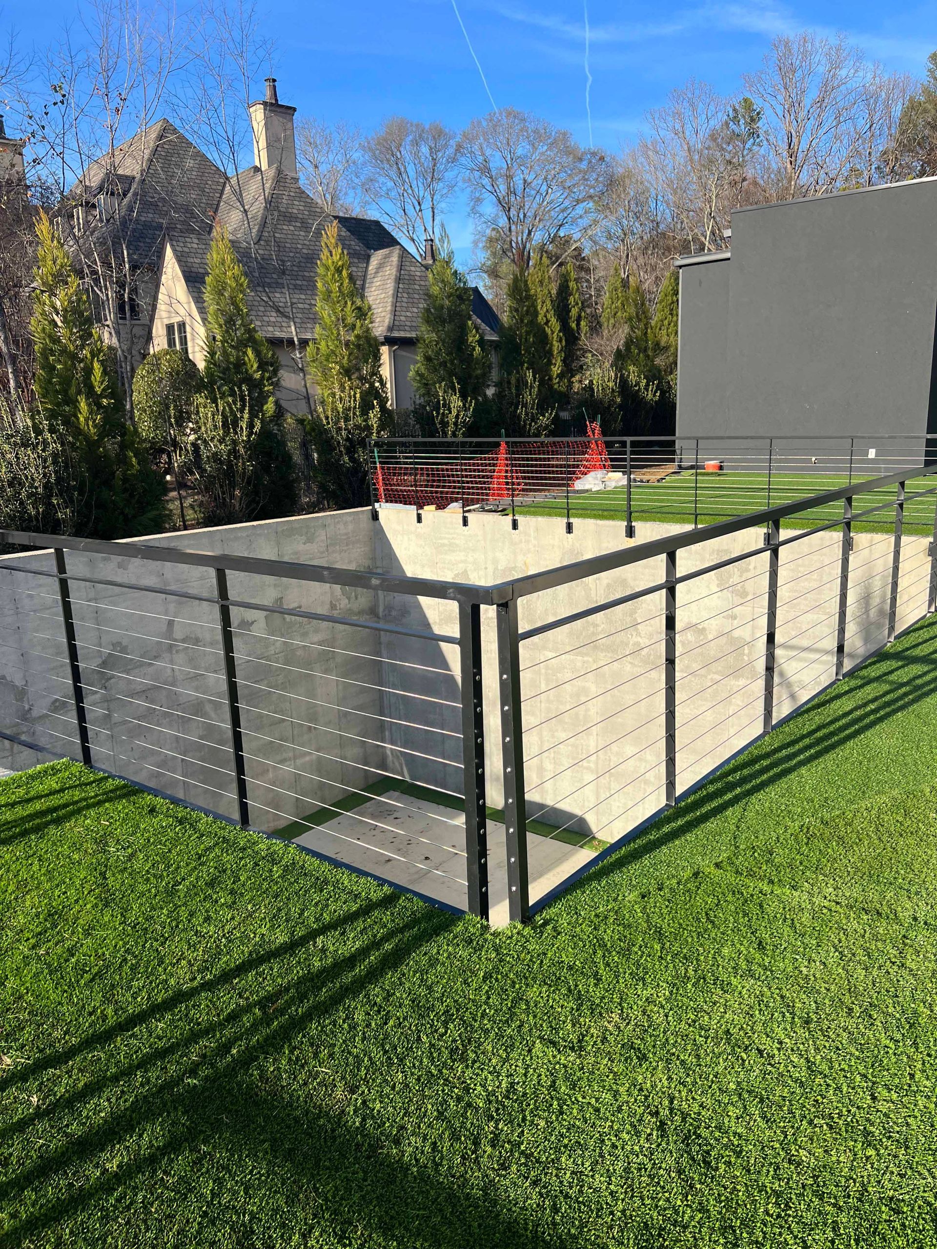 A fence surrounds a lush green field with a house in the background.