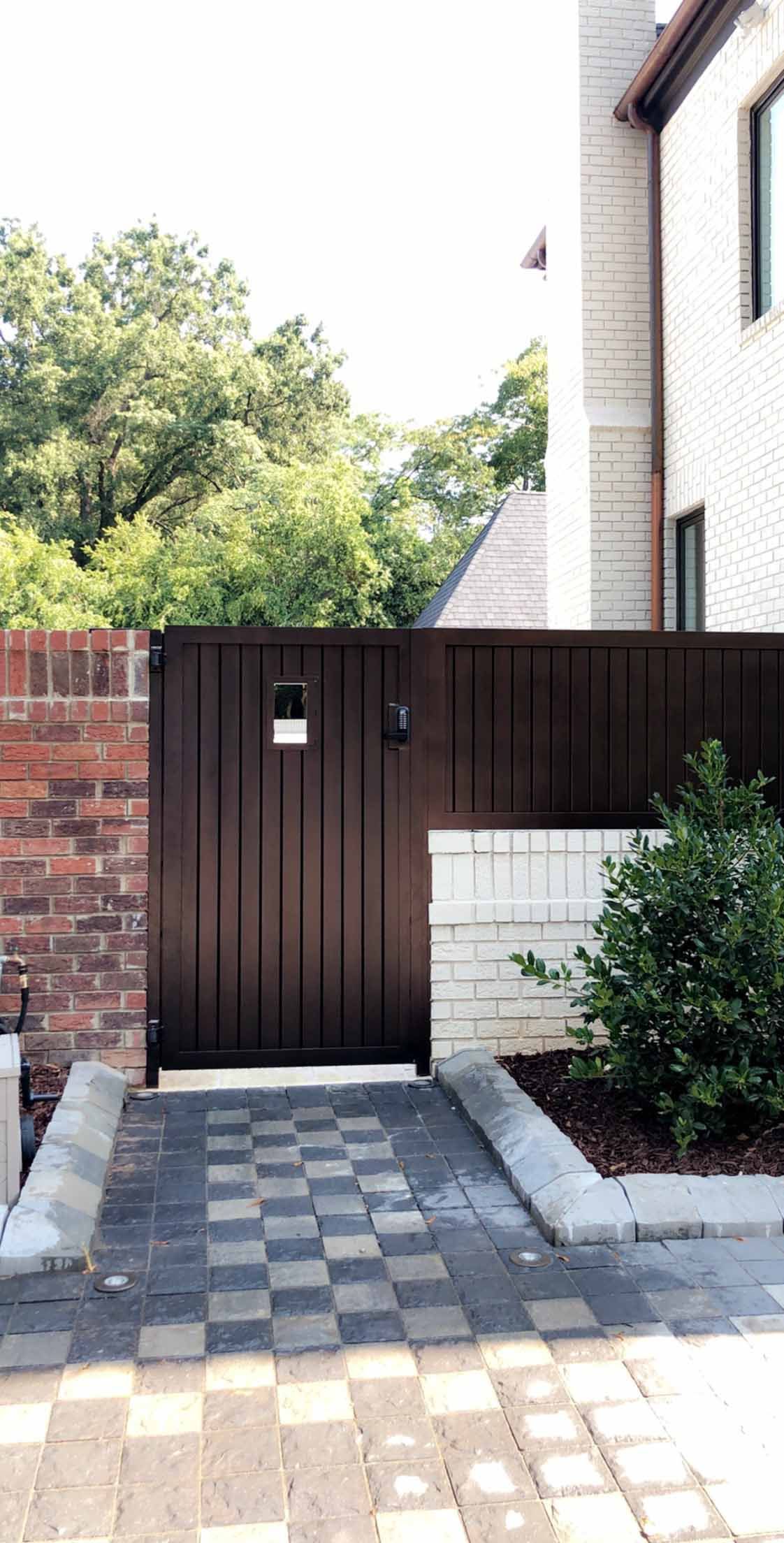 A wooden gate is leading to a house with a brick wall.