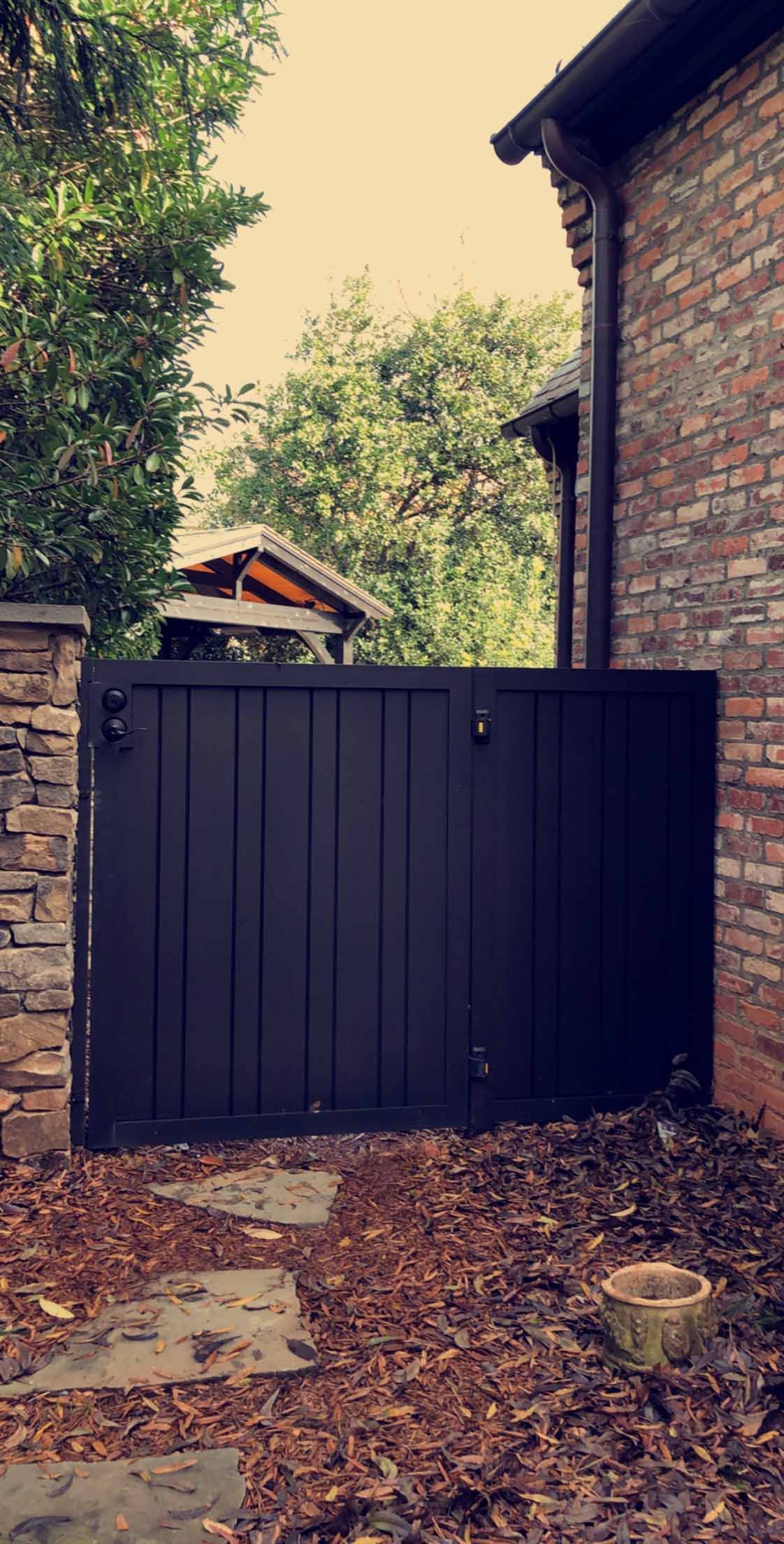 A black gate is sitting next to a brick building.