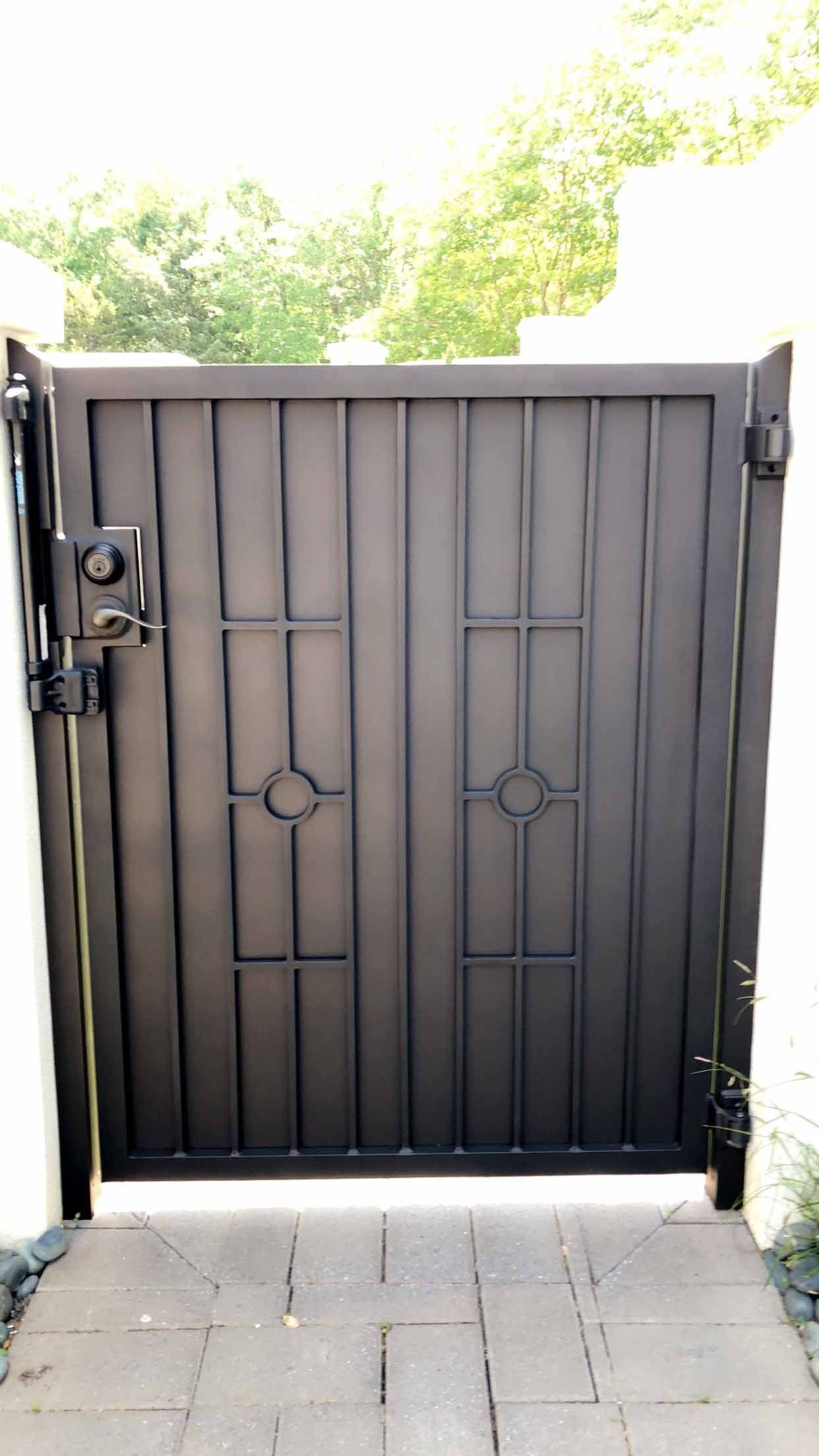 A black gate is sitting on a sidewalk next to a white wall.