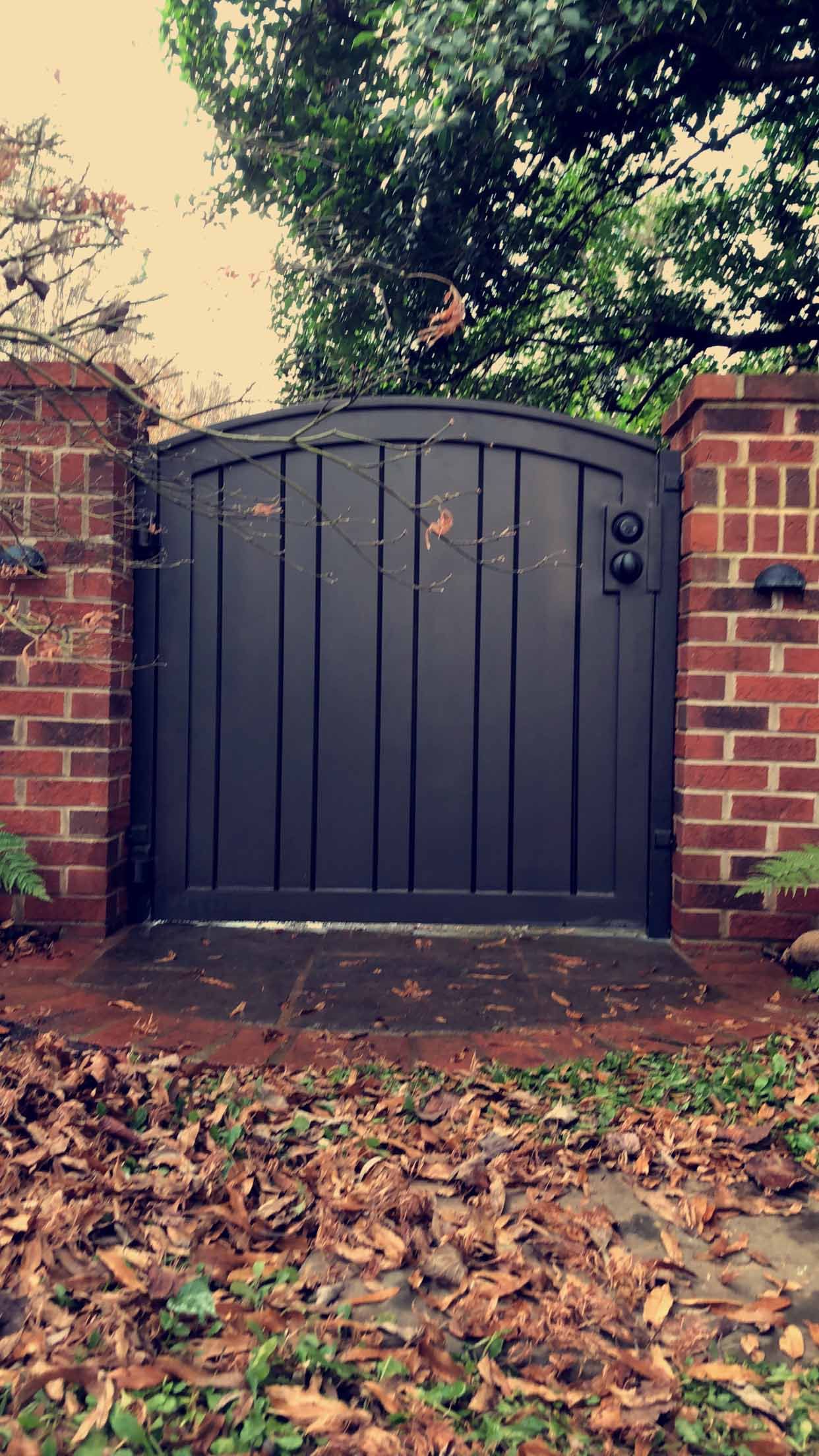 A black gate is sitting in front of a brick wall.