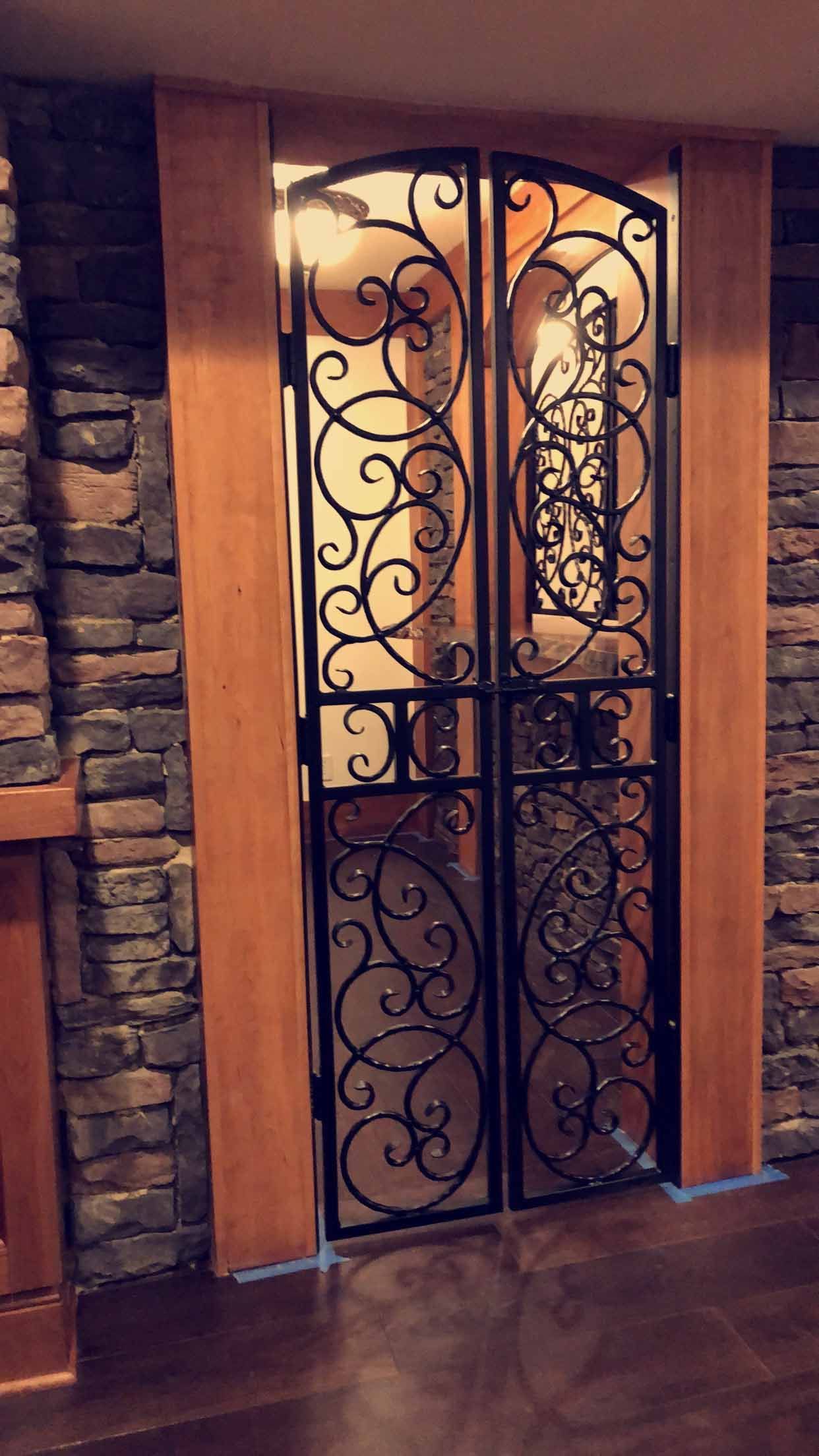 A wrought iron gate is in a room next to a stone wall.