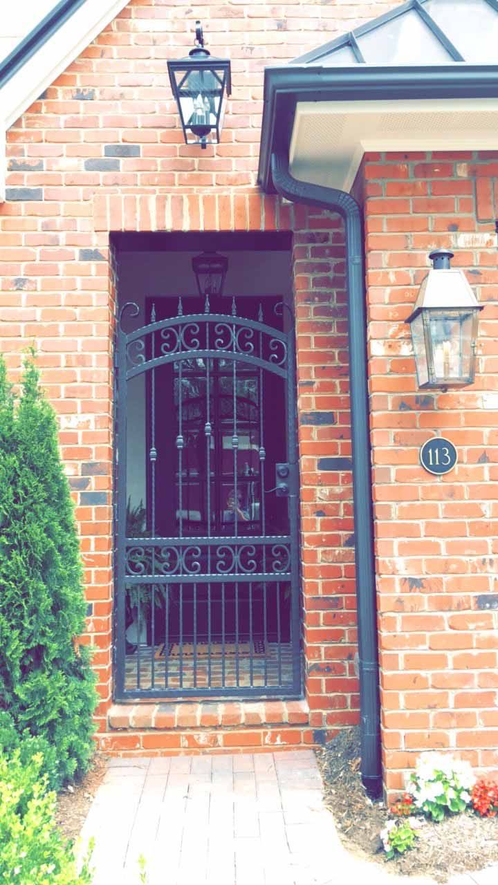 The front door of a brick house with a wrought iron gate.
