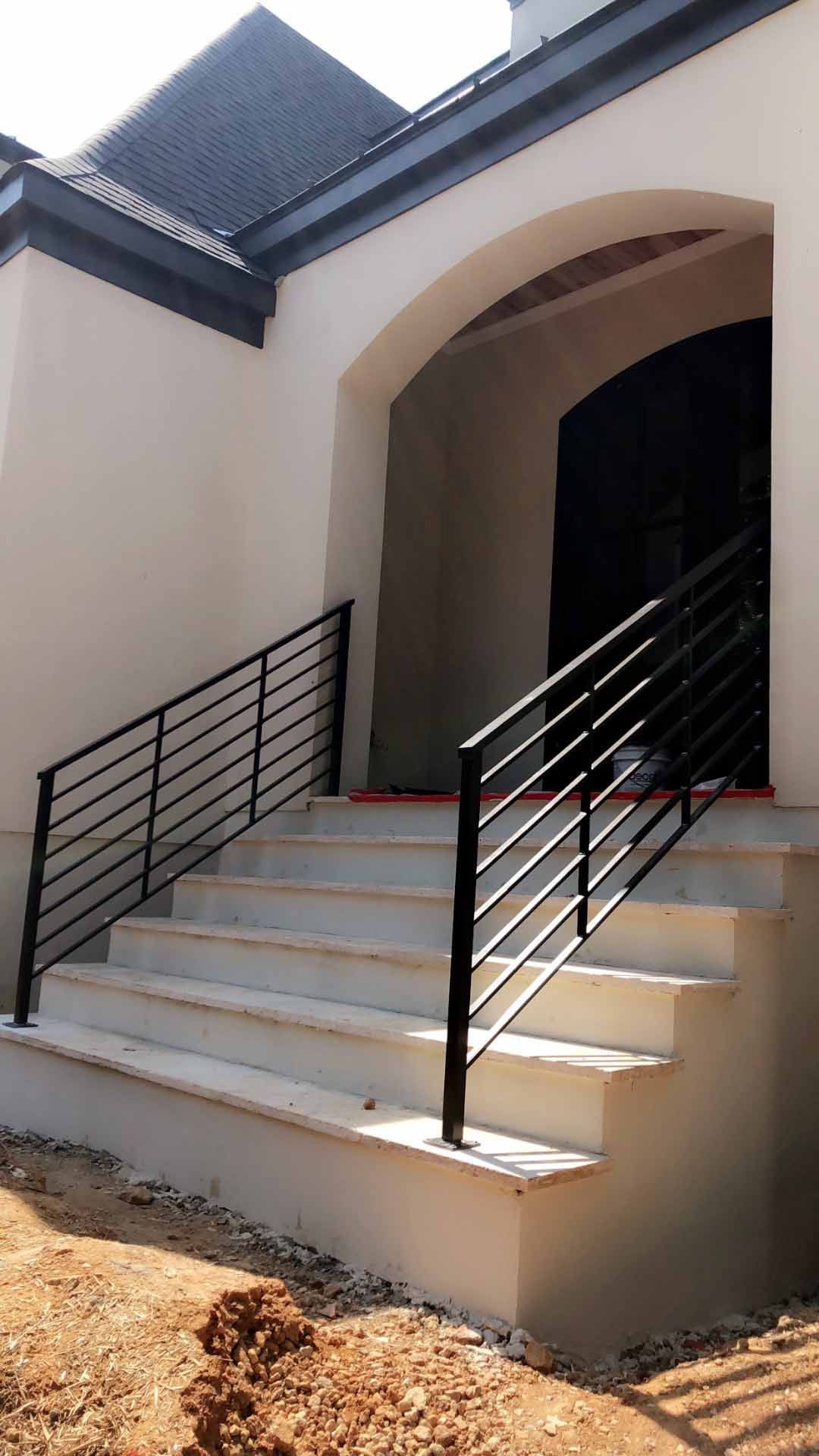 A white house with stairs and a black railing.