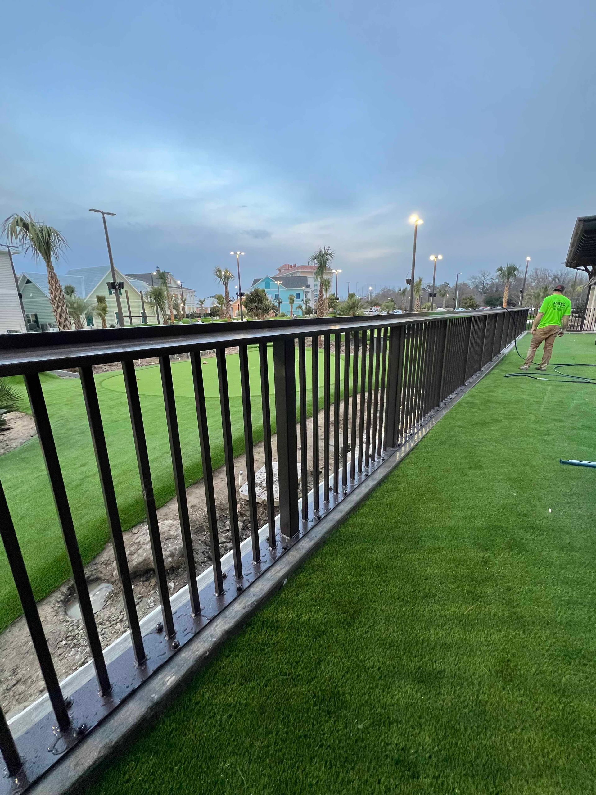 A person is playing golf in a park next to a fence.