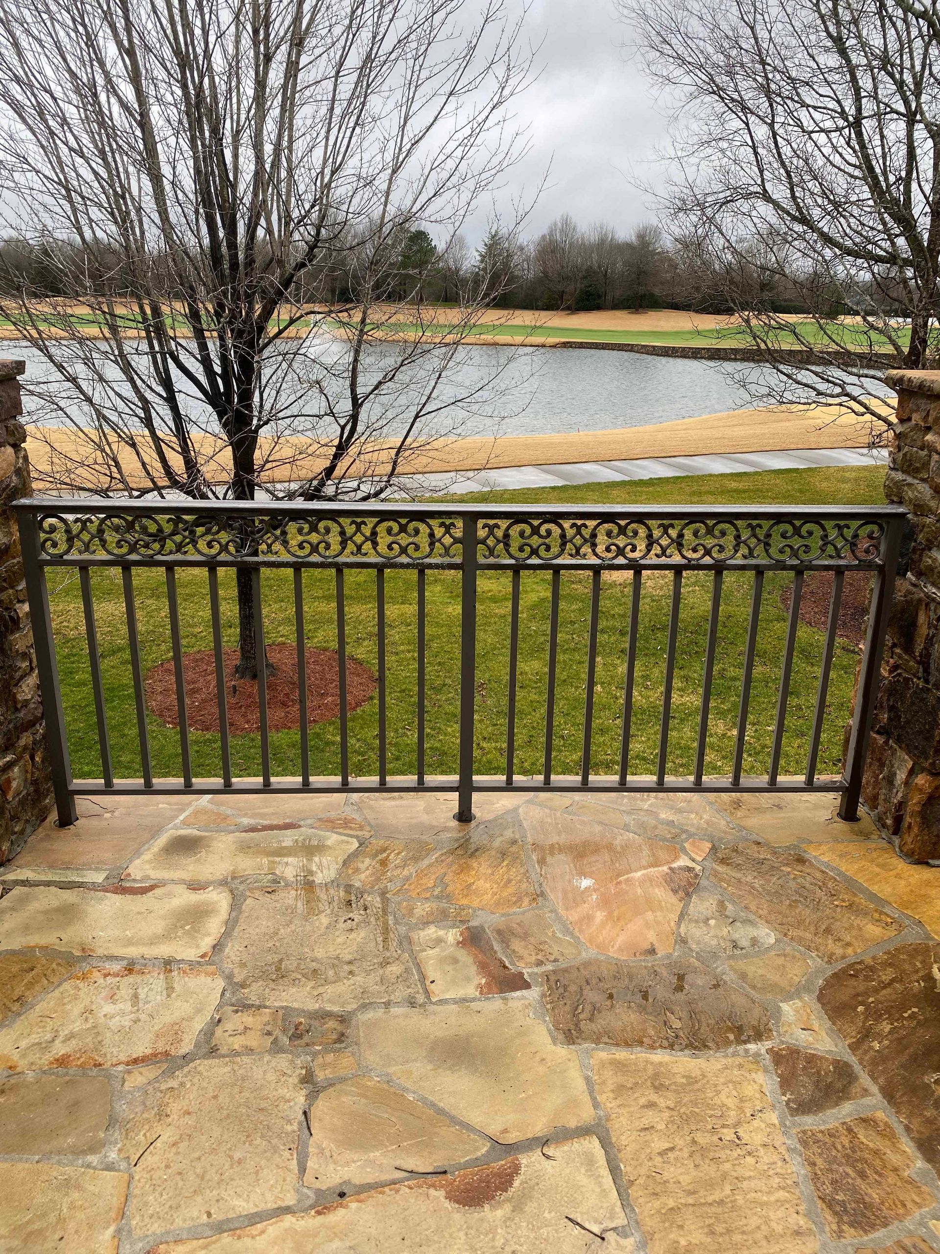 A stone patio with a metal railing overlooking a lake.