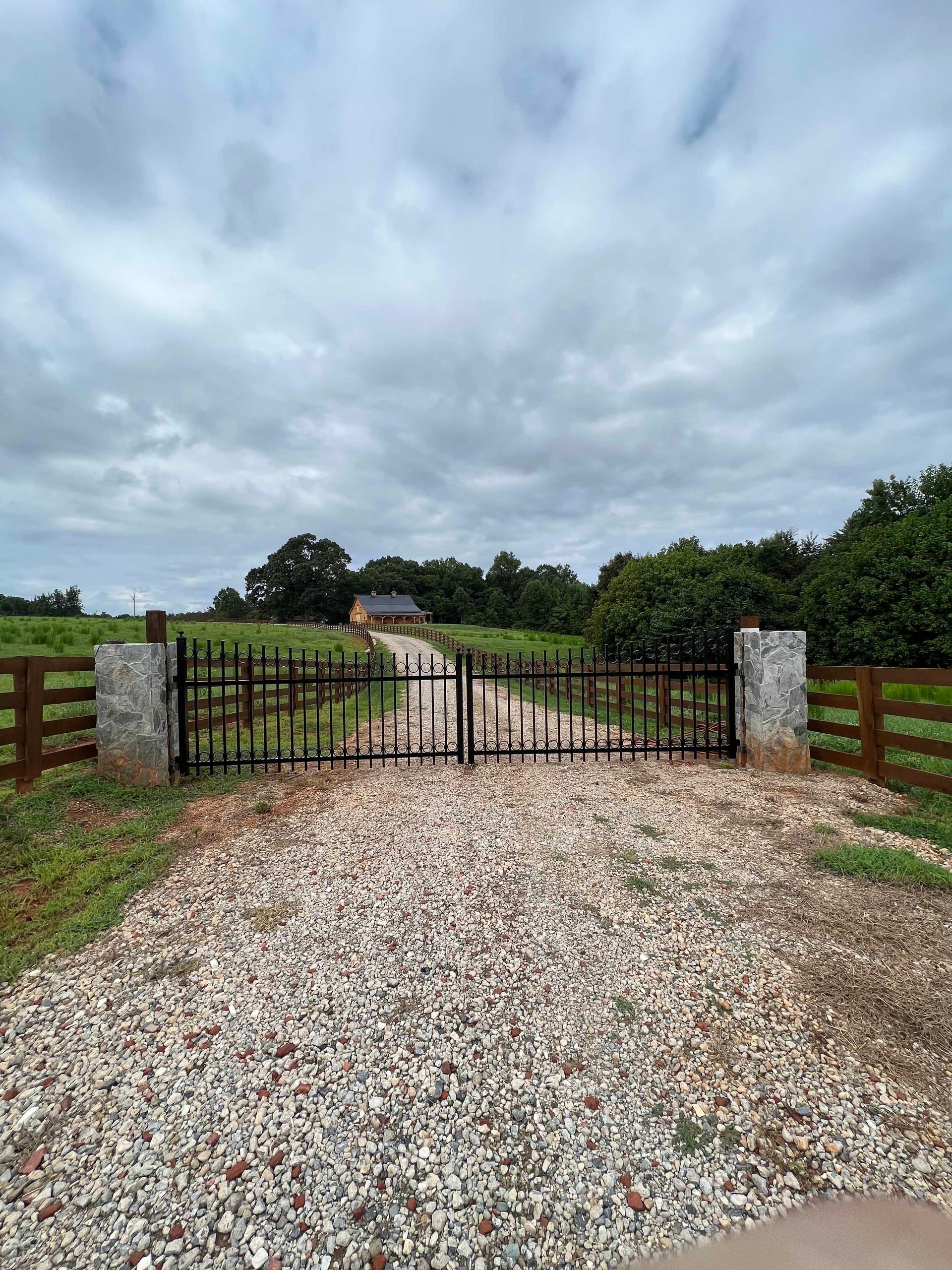 A gravel road with a gate in the middle of it leading to a house.