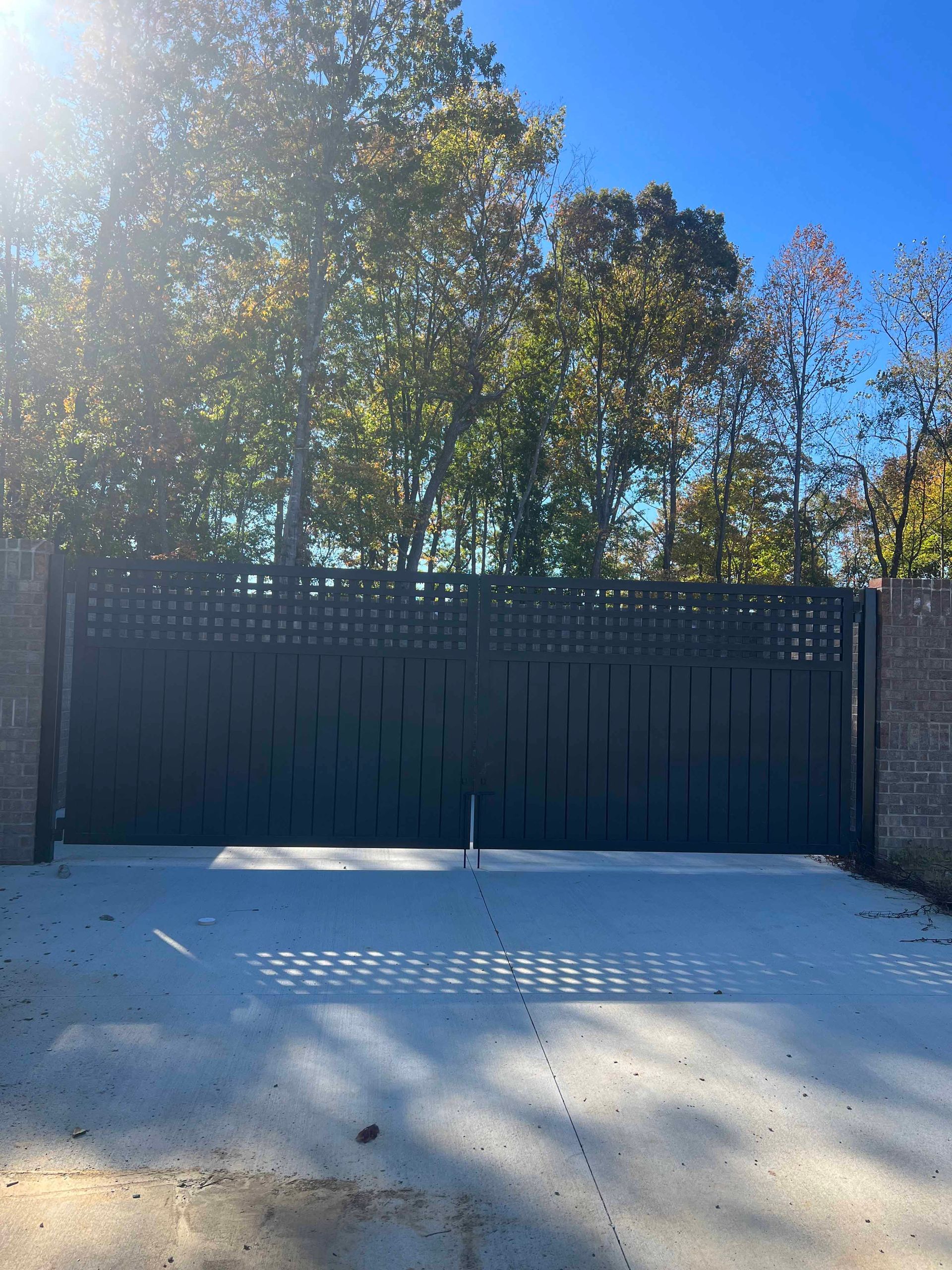 A black gate is surrounded by trees and a brick wall.