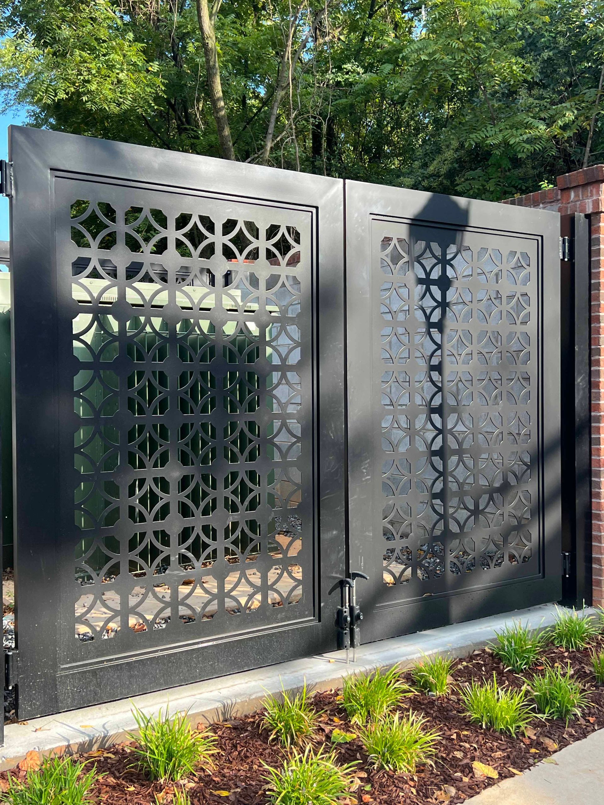 A black gate with a pattern on it is sitting next to a brick wall.