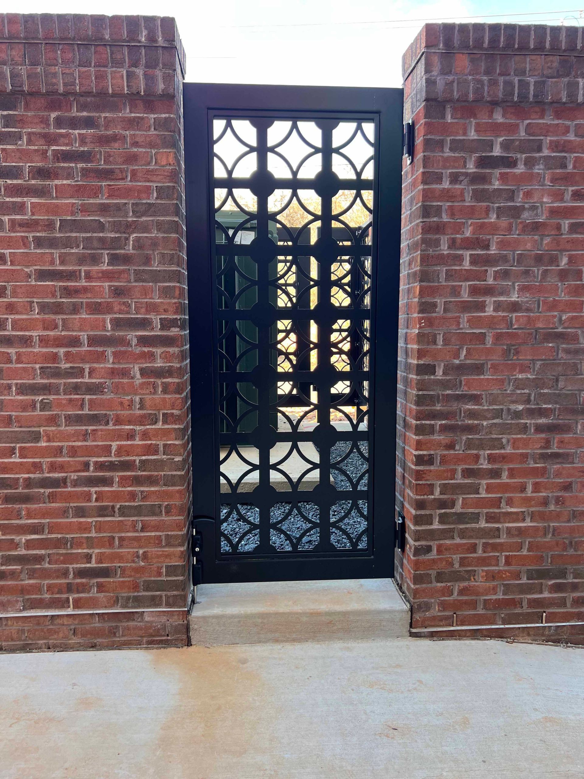 A black gate with a brick wall behind it