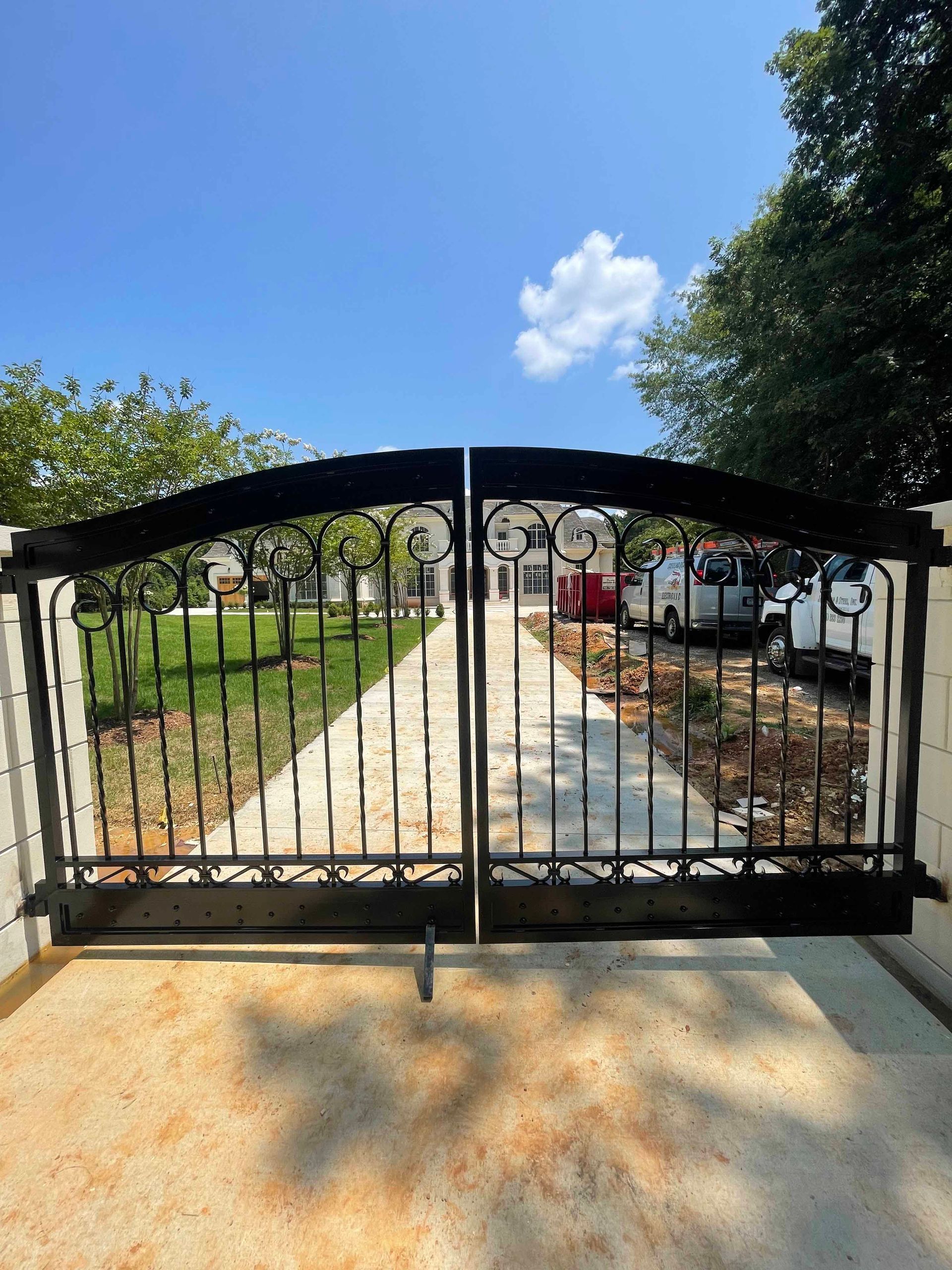 A wrought iron gate is open to a driveway leading to a house.