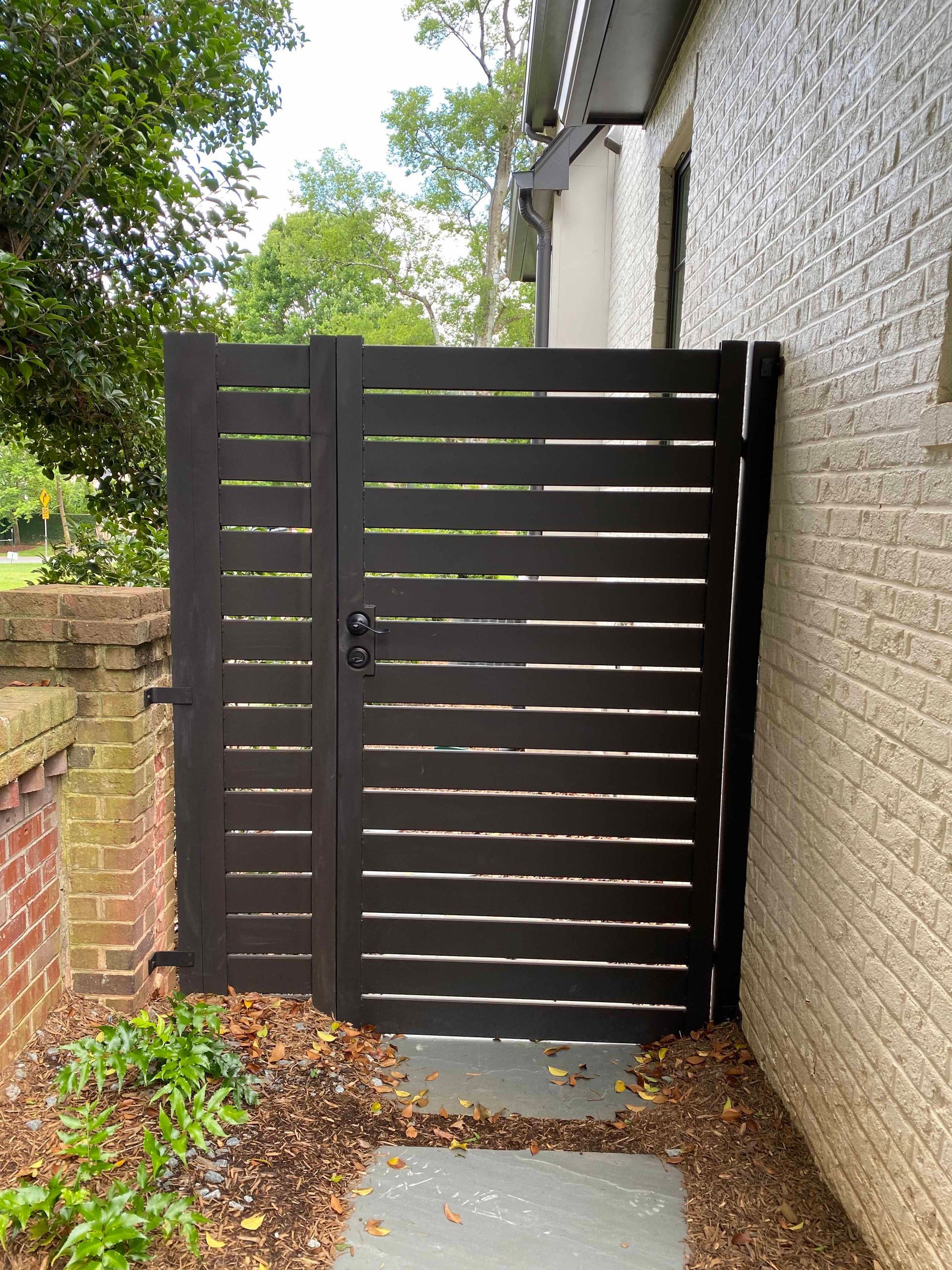 A black gate is sitting on the side of a brick building.
