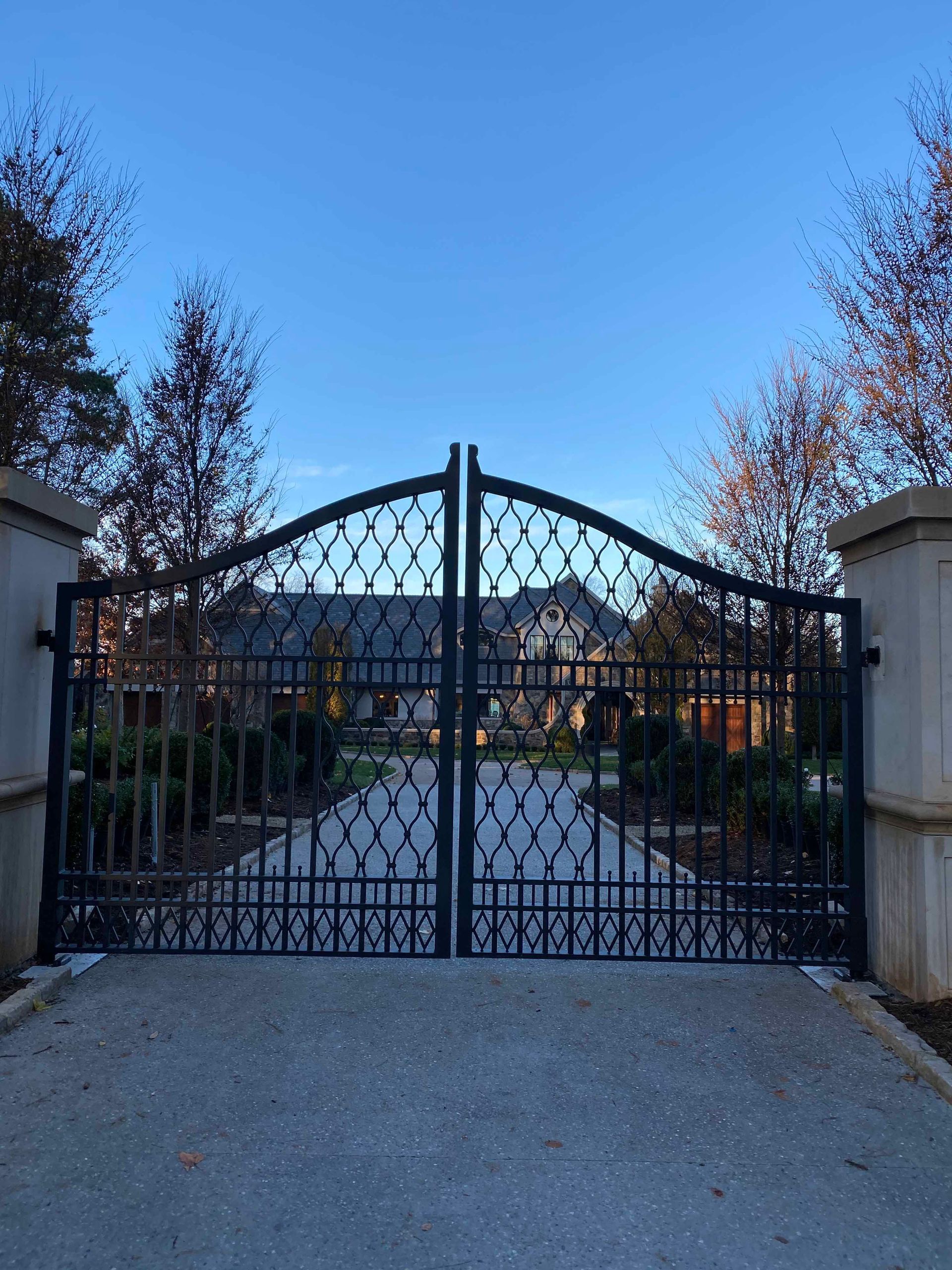 A wrought iron gate is open to a driveway leading to a house.