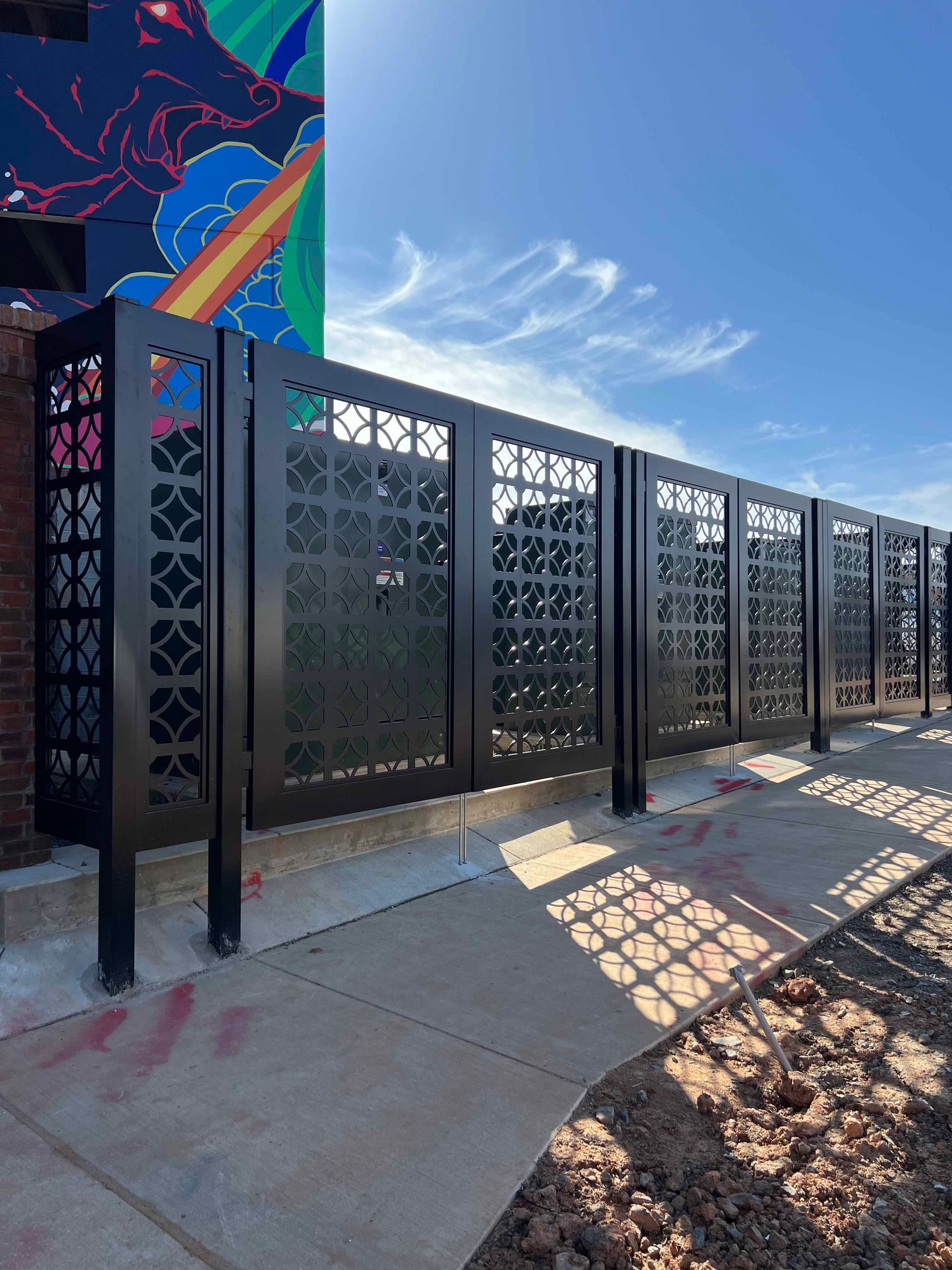 A fence with a mural on the side of a building in the background.