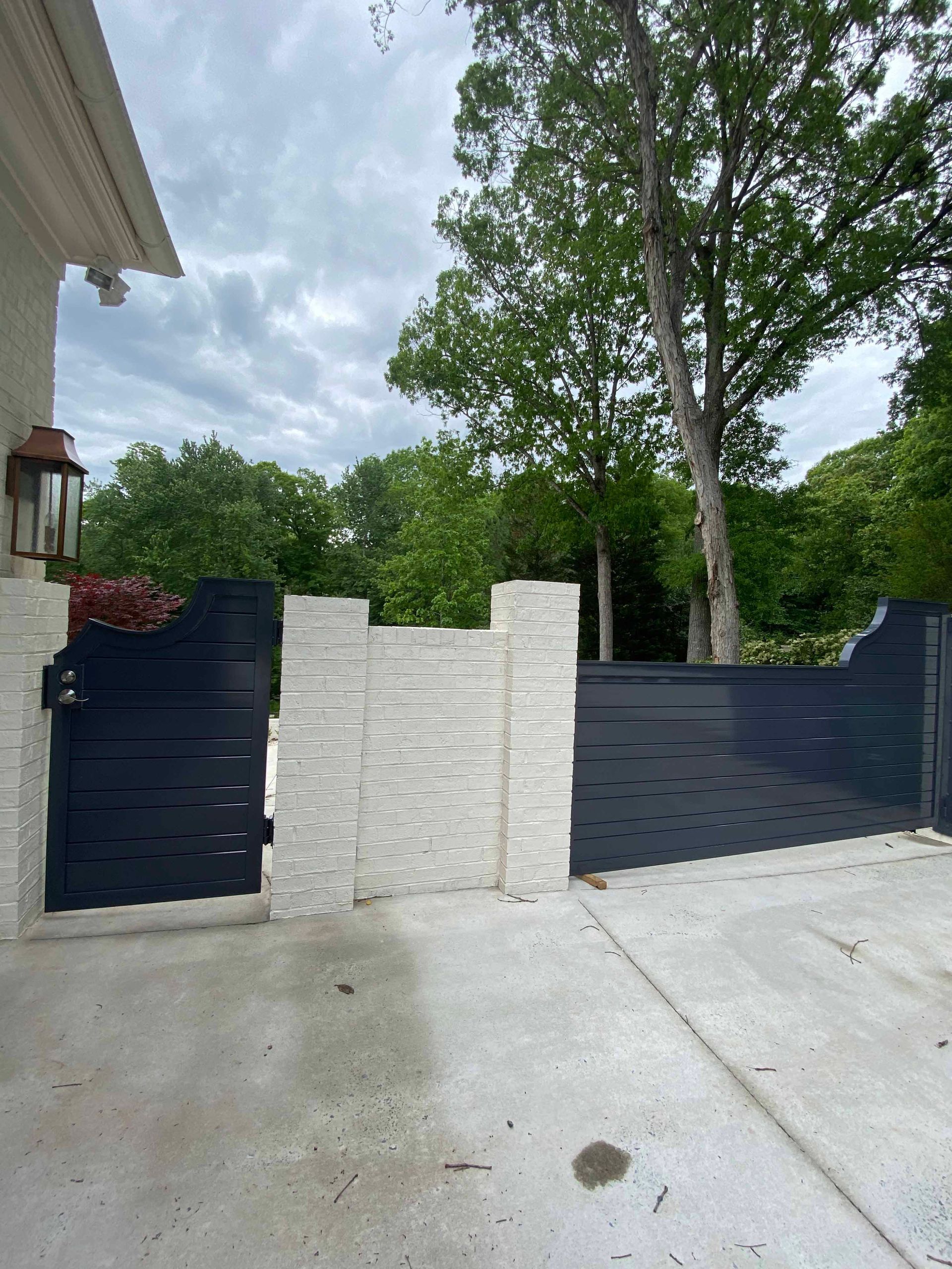 A black gate is sitting in front of a white brick wall.