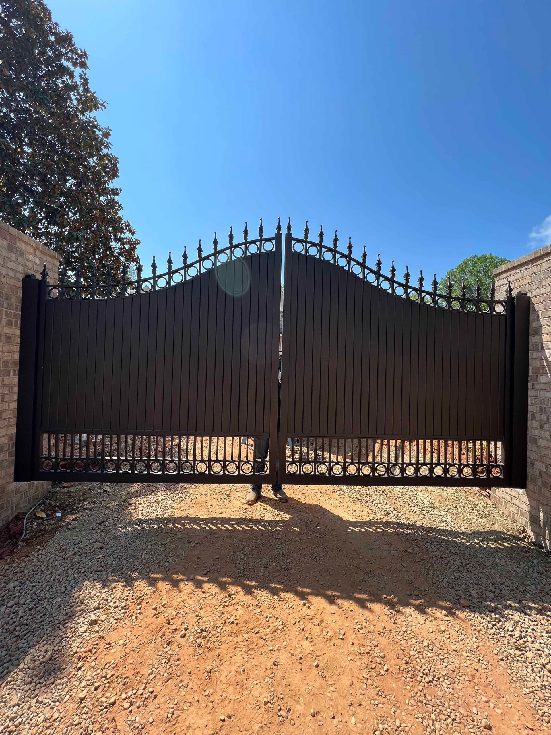 A black gate is sitting on top of a gravel driveway.