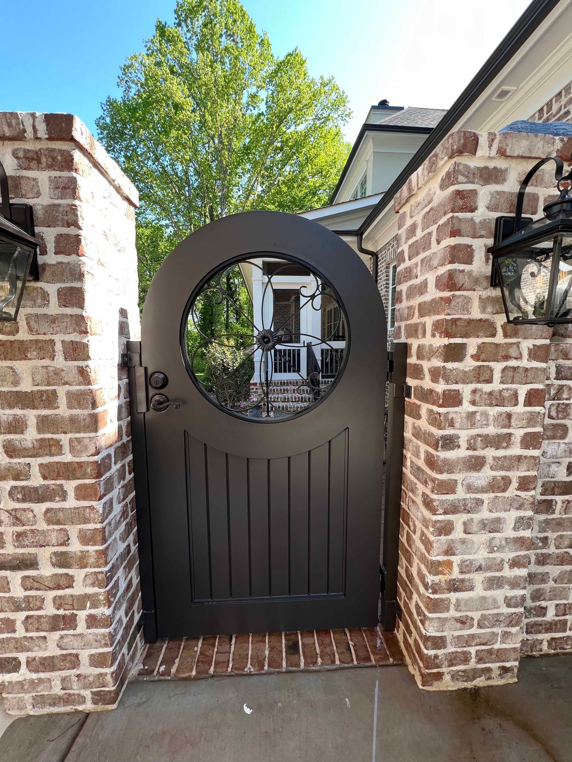 A black gate with a round window is surrounded by brick pillars.