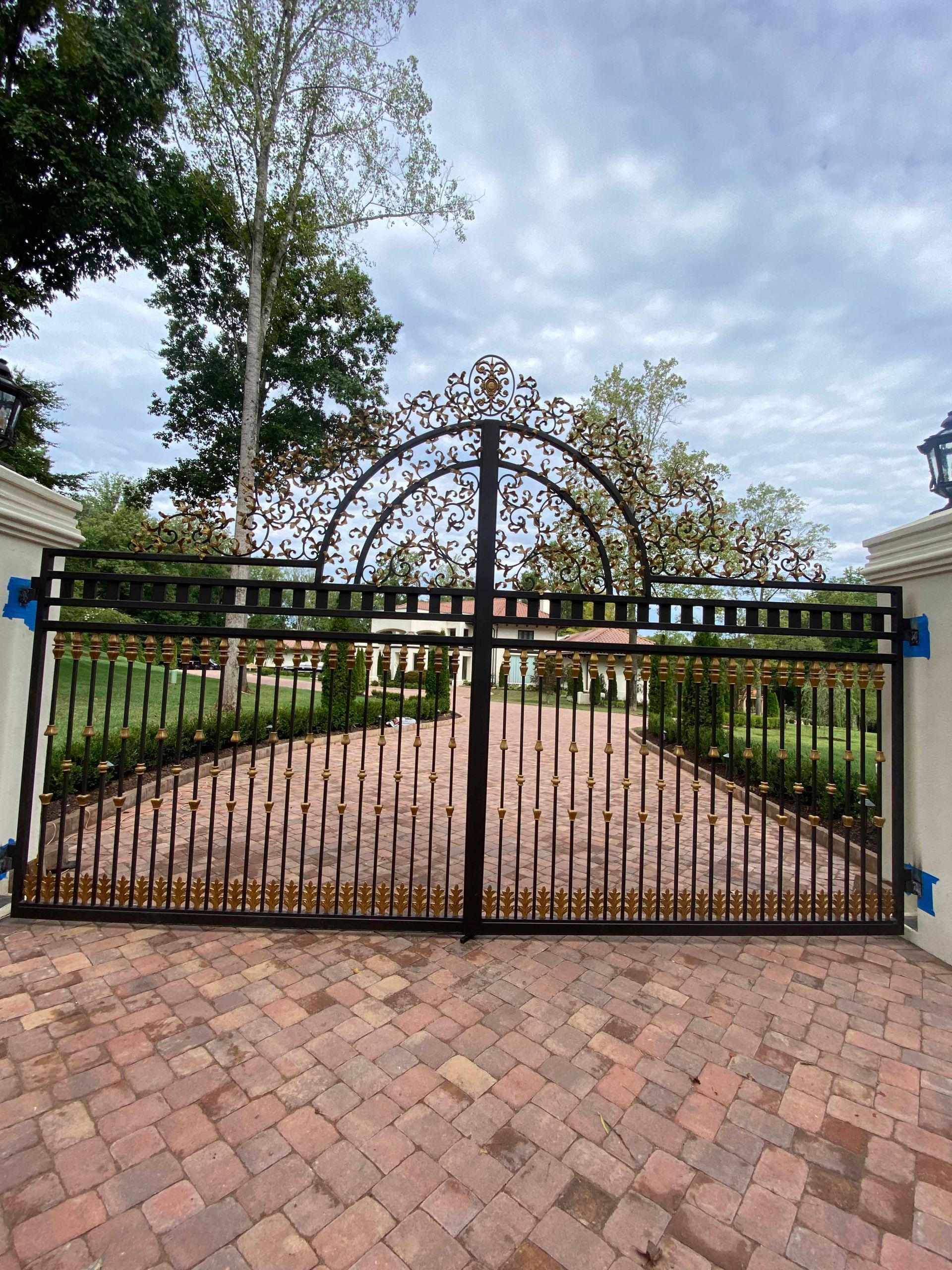 A wrought iron gate with a brick driveway in front of it