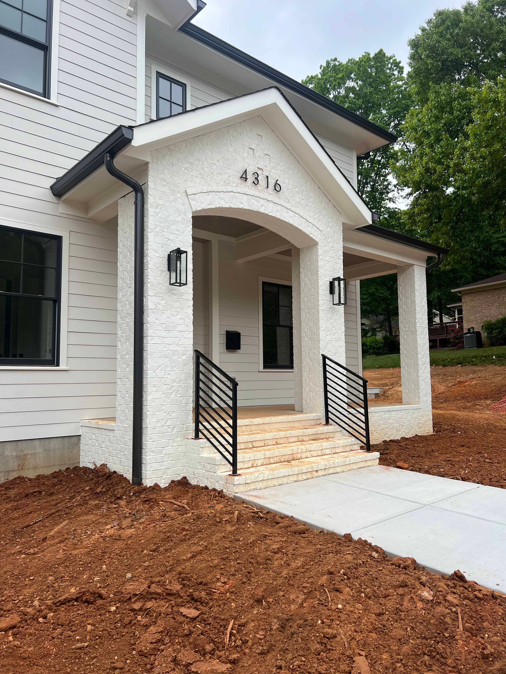 A white house with a porch and stairs is sitting on top of a dirt hill.