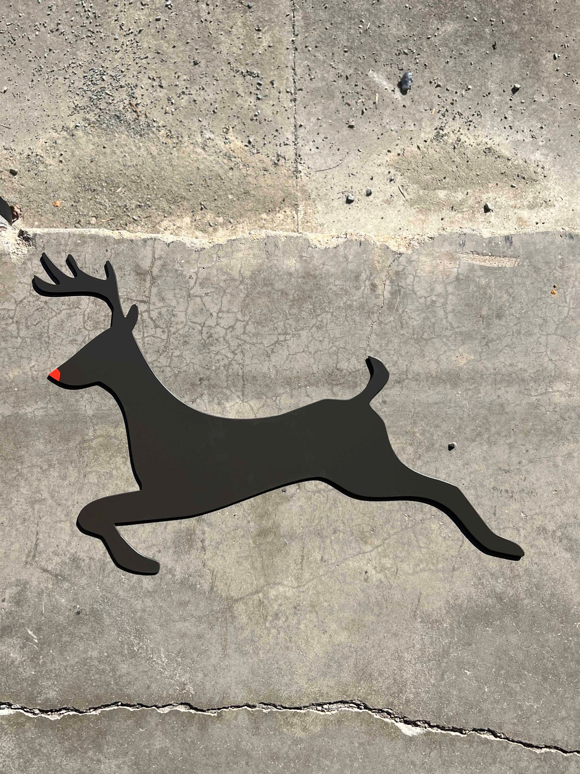 A black reindeer with a red nose is running on a concrete surface.
