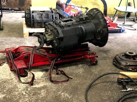 A transmission is sitting on top of a red jack in a garage.