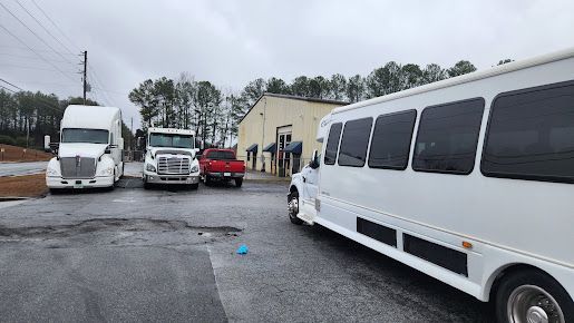 A white bus is parked in a parking lot next to a truck.