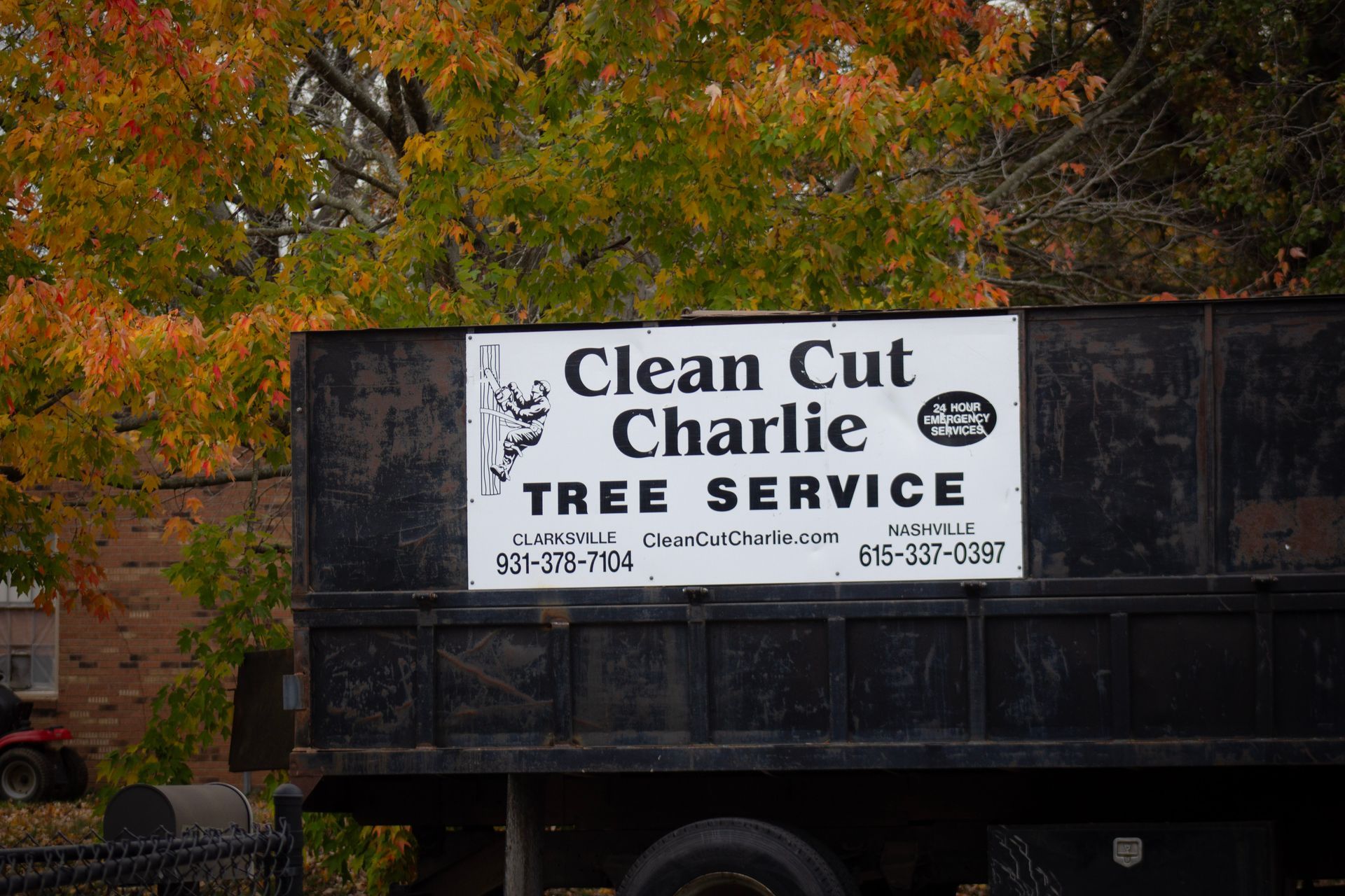 Clean Cut Charlie Tree Service truck with sign. Autumn foliage background.
