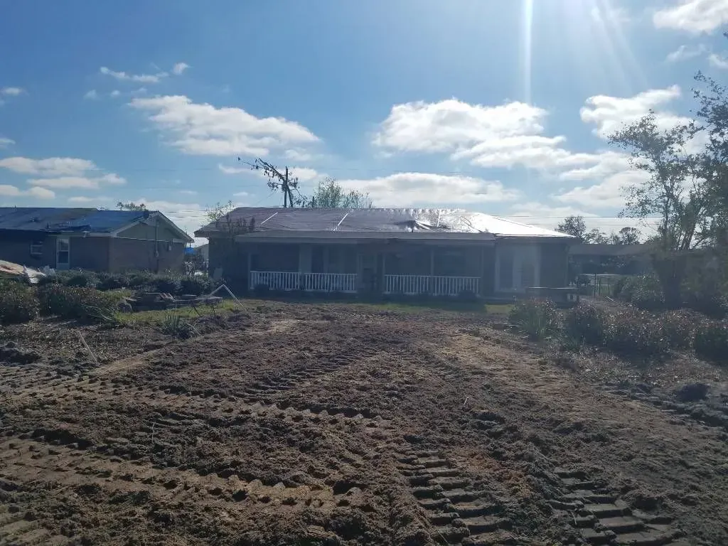 House under construction on a dirt lot; bright blue sky and sun.