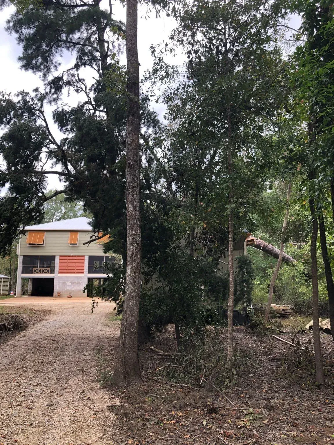 Gravel driveway leads to two-story house with covered porch. Trees and brush surround the building.