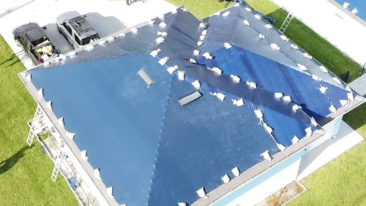 Blue roof partially covered in solar panels, surrounded by grass and parked vehicles.