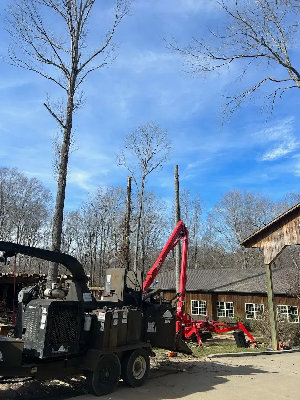 Wood chipper near a building with bare trees and a blue sky.