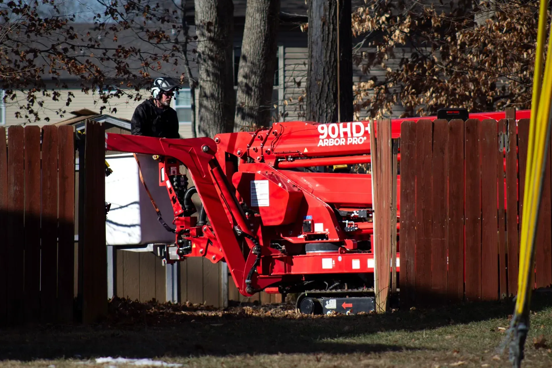 Red tree trimming machine with operator, working within a wooden fence.