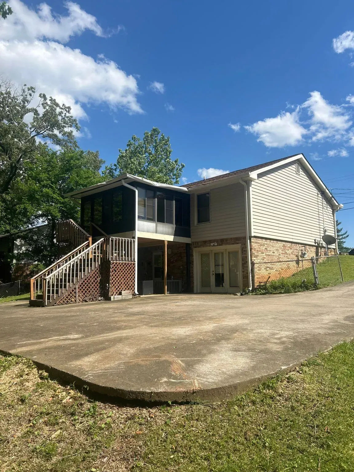 Two-story house with a screened porch and a paved driveway, set against a blue sky with clouds.