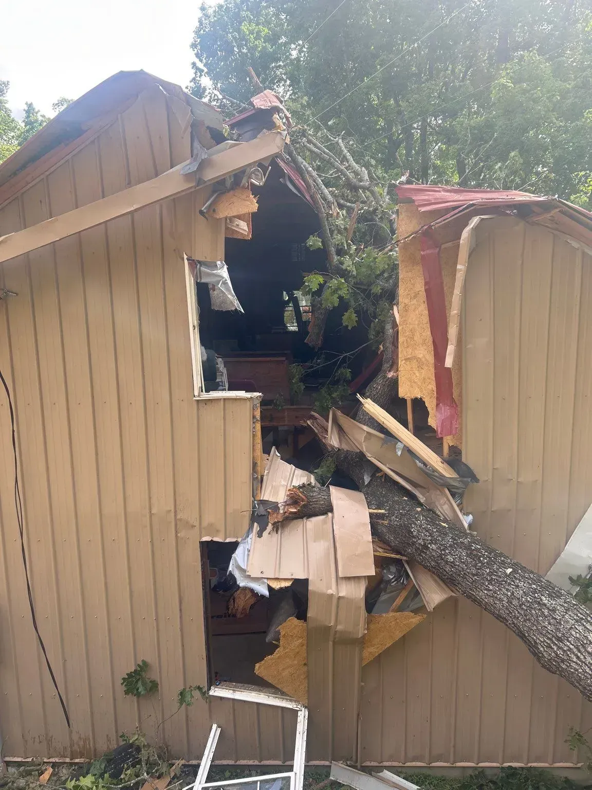 A tree crashed into a tan-sided building, causing extensive damage to the roof and walls.