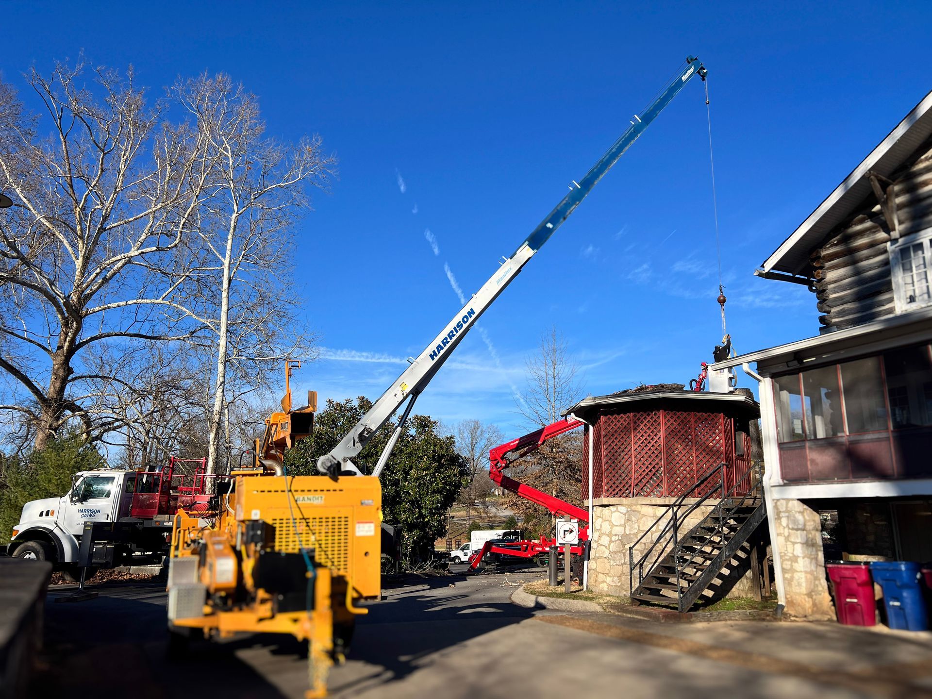 A tree service removing branches near a building; a yellow wood chipper and truck are visible.