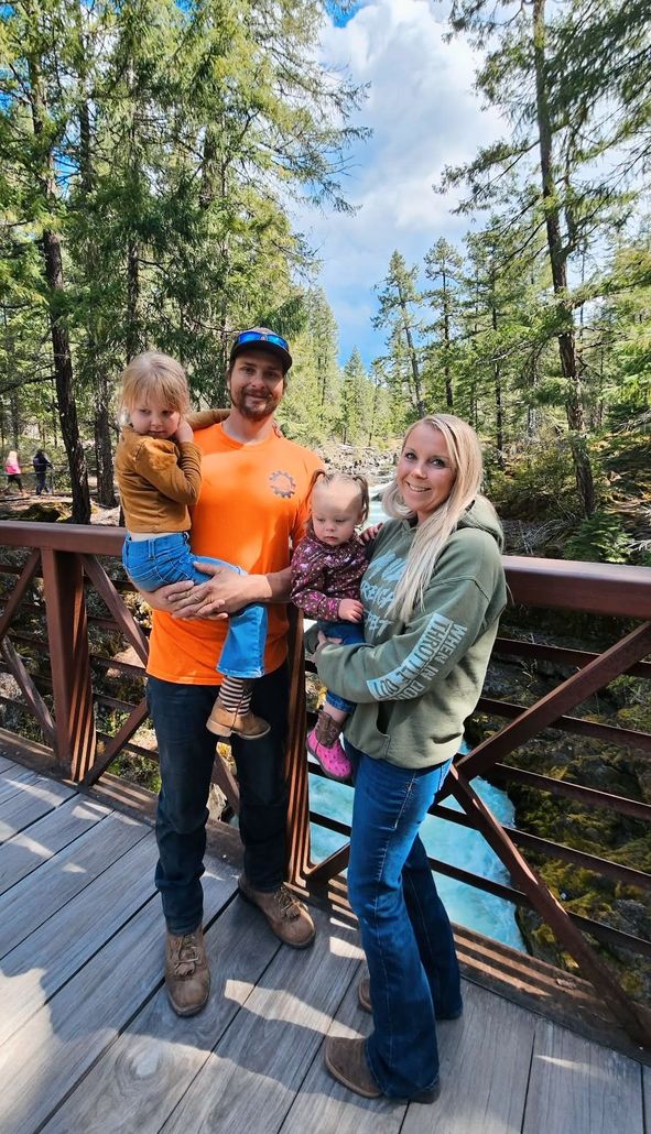 Family of four posing on a wooden bridge in a forest, with two children and two adults smiling.