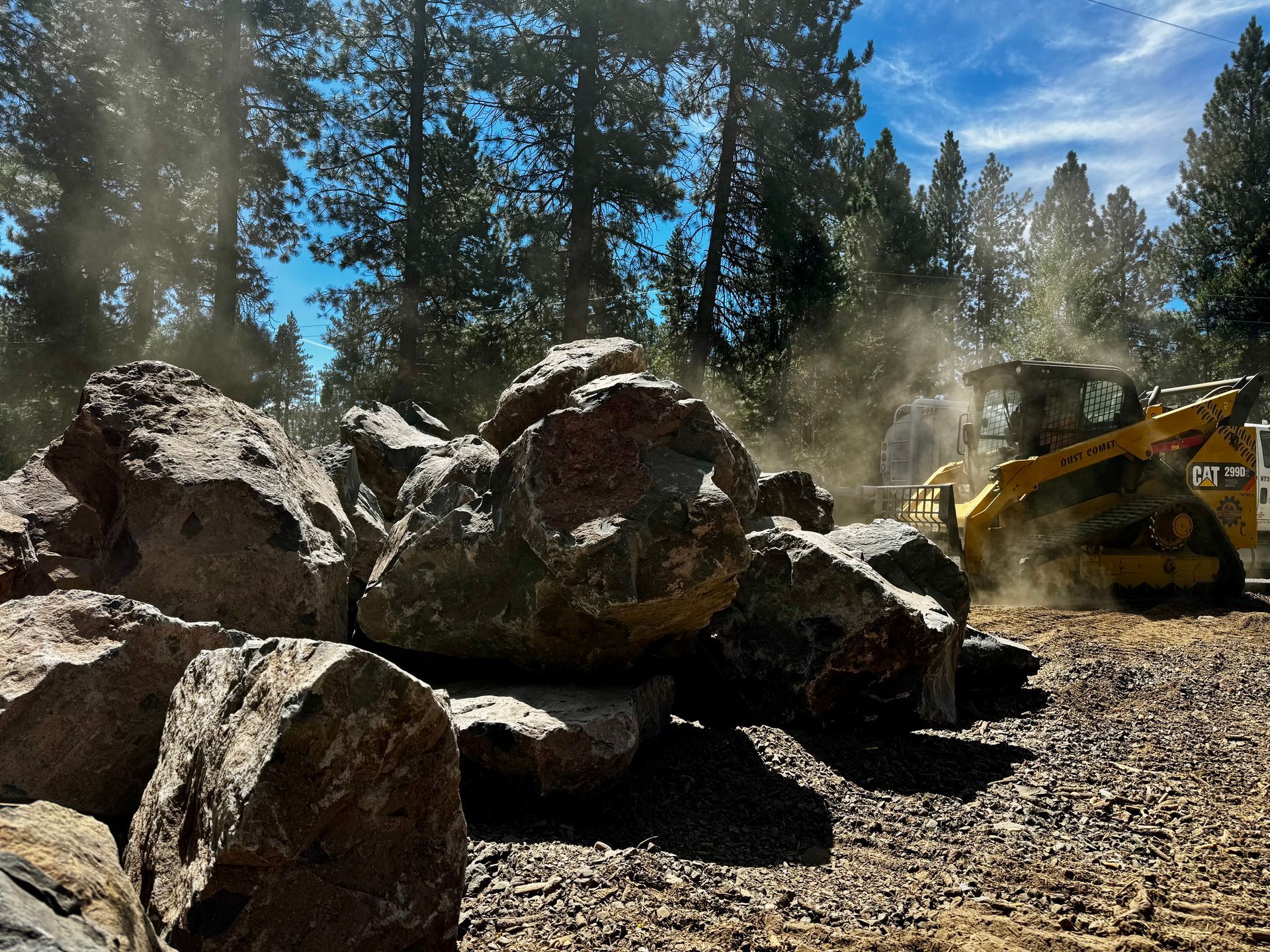 Bulldozer moving huge rocks at a dusty forest worksite under a blue sky